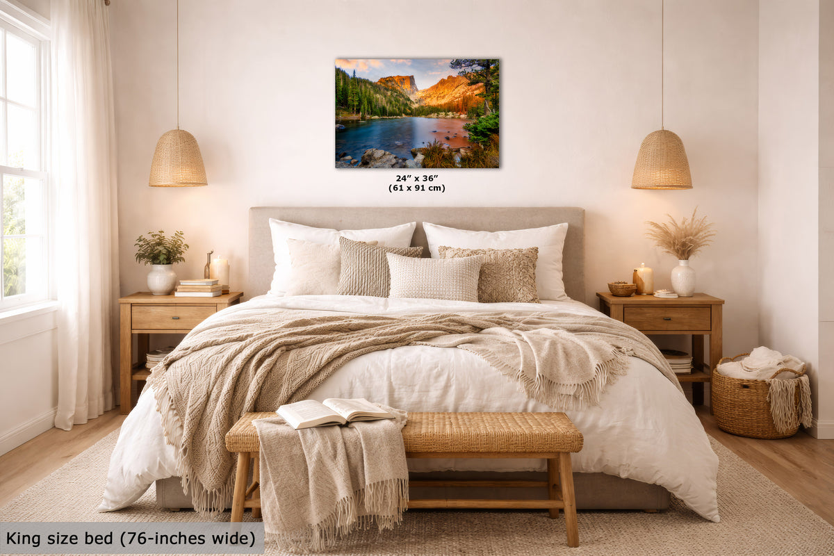 A landscape wall art print showing a colorful mountain lake scene, displayed above a neatly made bed in a bright, modern bedroom. The print includes size text indicating 24 x 36 inches (61 x 91 cm).