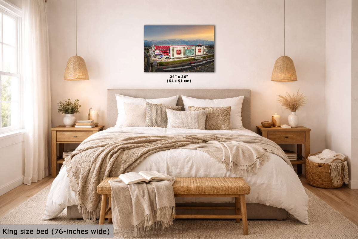 A San Francisco 49ers Stadium art print, displayed above a neatly made bed in a bright, modern bedroom. The print includes size text reading 24 x 36 inches (61 x 91 cm), and the room scene includes a bed, nightstands, lamps, and decorative textiles.