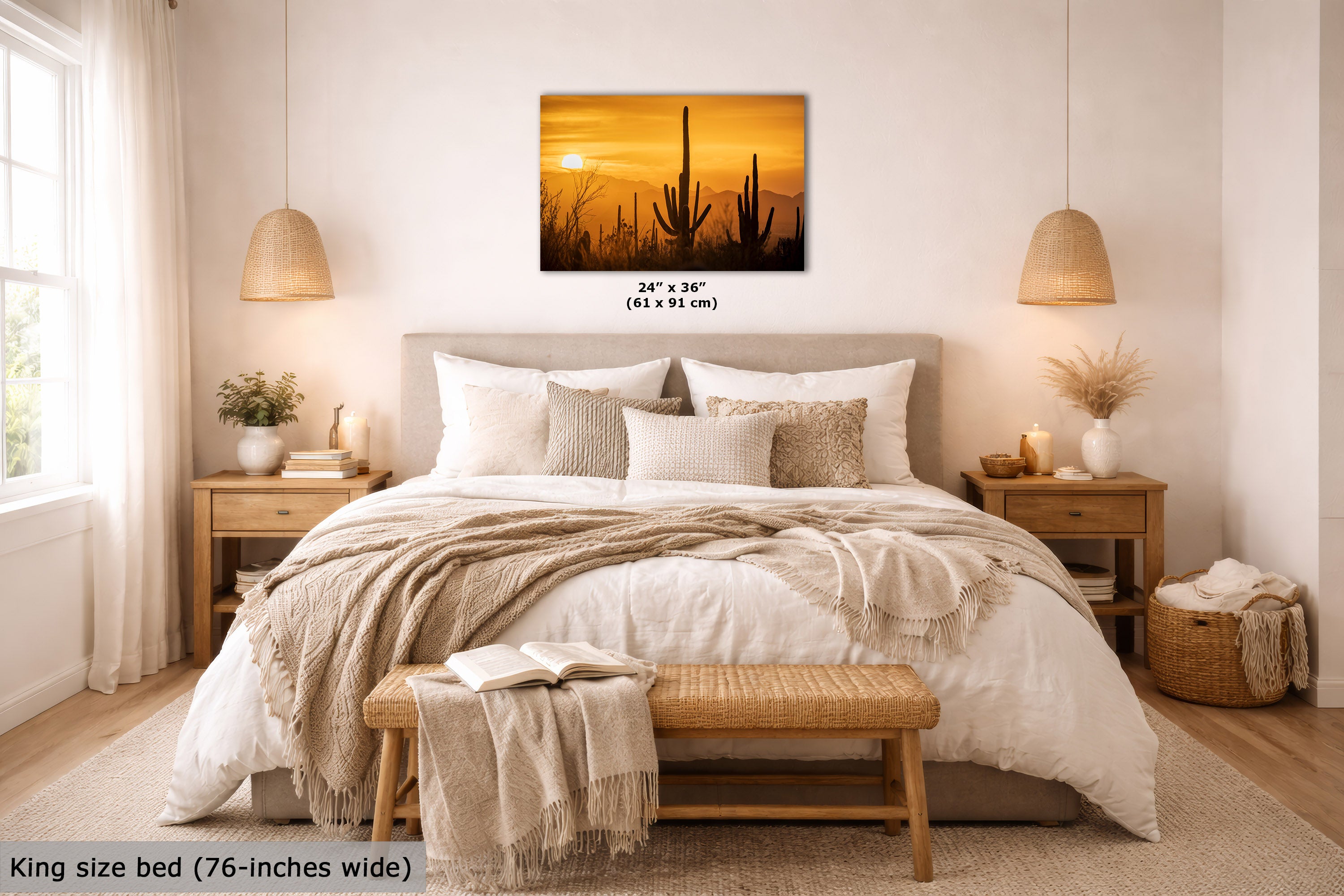 A wall art print showing a desert sunset with saguaro cacti, displayed above a neatly made bed in a bright, modern bedroom. The print includes size text reading 24" x 36" (61 x 91 cm), and the scene is labeled as a lifestyle interior mockup.
