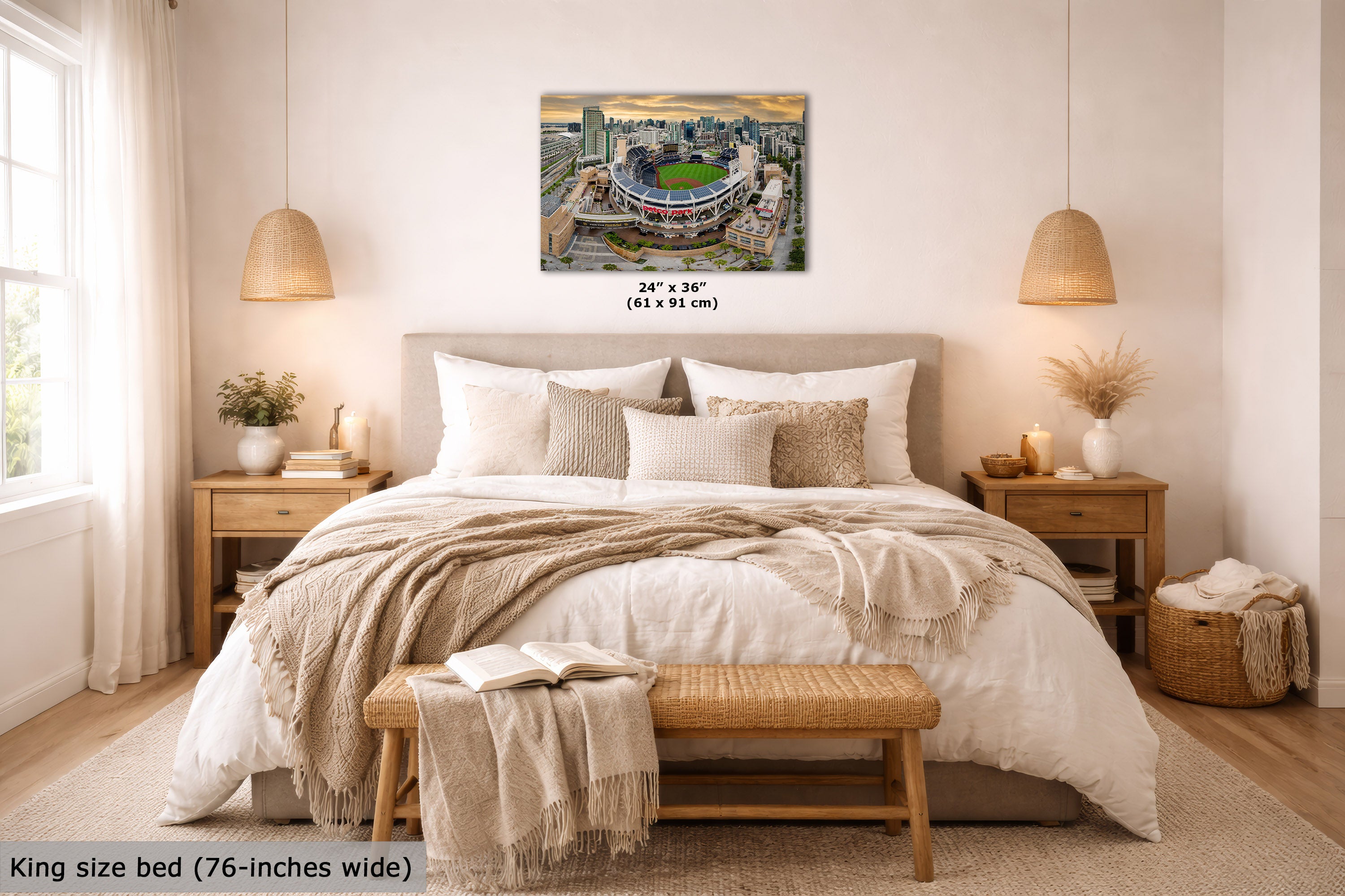 A wall art print showing an aerial view of a stadium and surrounding cityscape, displayed above a neatly made bed in a warm, modern bedroom. The print includes size text reading 24 x 36 inches (61 x 91 cm) and a caption at the bottom left stating King size bed (76-inches wide).
