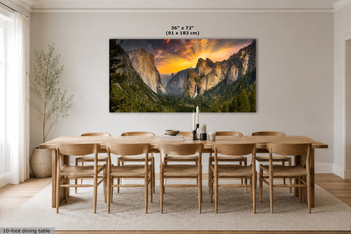 A large rectangular wall art print showing a mountain valley landscape at sunset, displayed above a wooden dining table and chairs in a bright modern dining room. Text above the artwork indicates dimensions 36 x 72 in (91 x 183 cm).