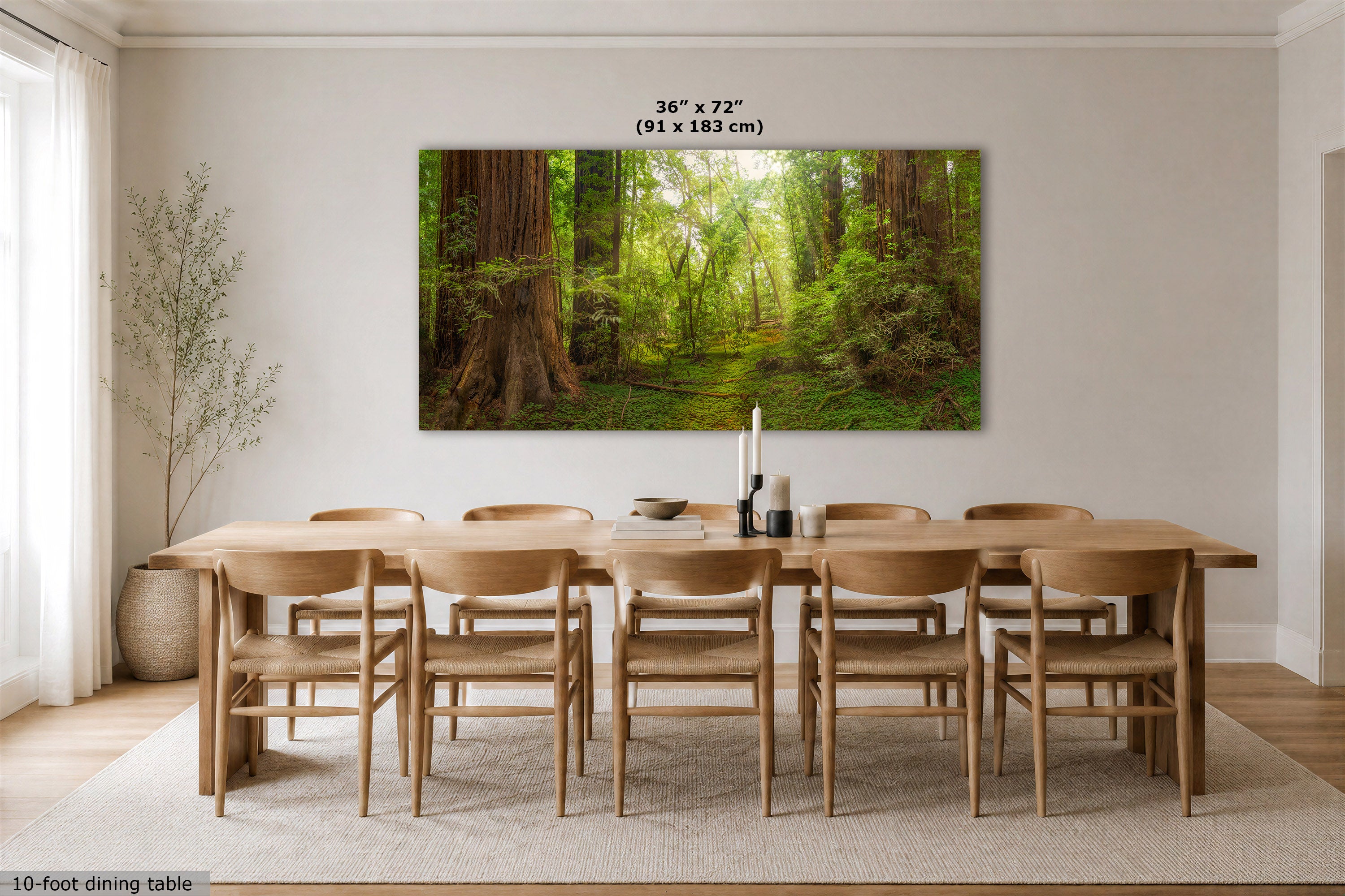 A large rectangular wall art print showing a sunlit forest path with tall trees and green foliage, displayed above a wooden dining table and chairs in a bright dining room. Text above the artwork reads 36 x 72" (91 x 183 cm).