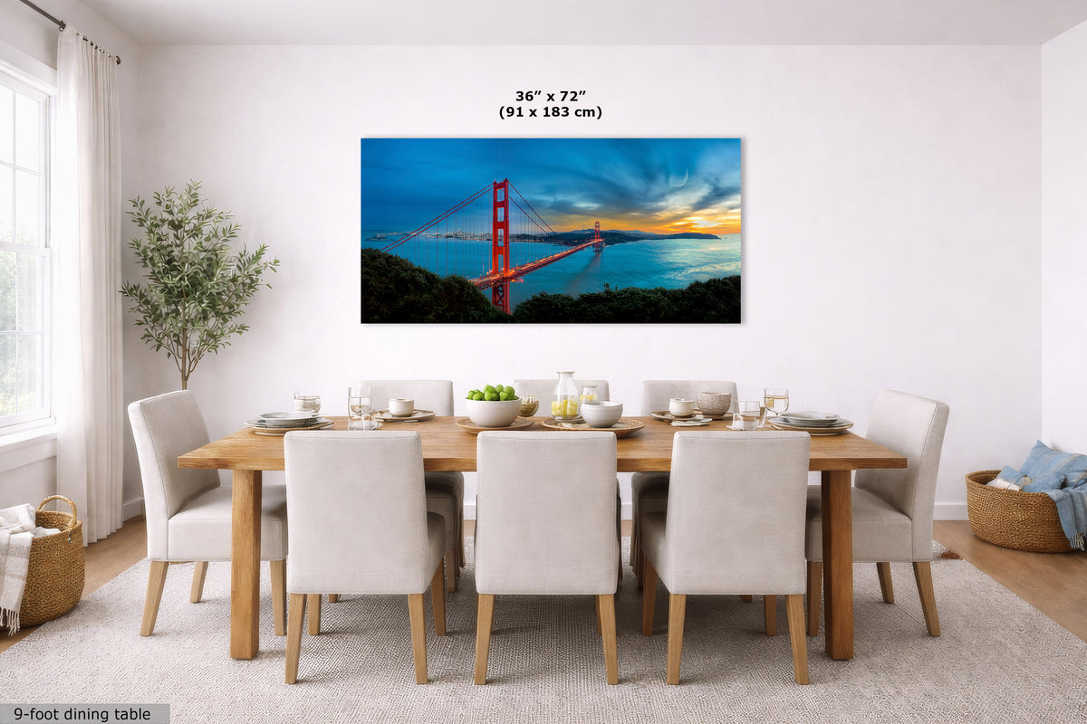 A framed wall art print depicting the Golden Gate Bridge over water at sunset, displayed above a dining table in a bright modern dining room. The print includes size text reading 36 x 72 inches (91 x 183 cm).