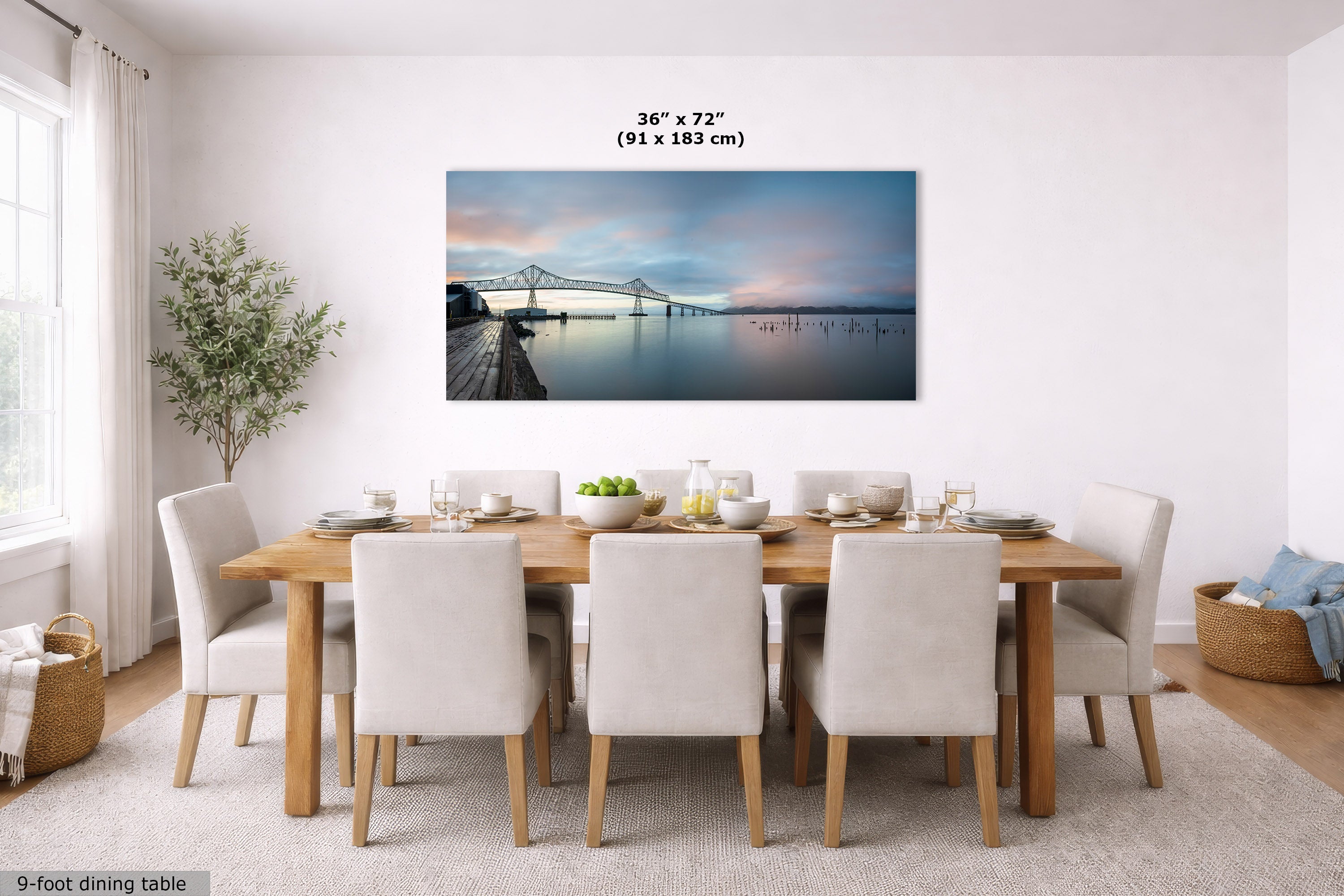 A framed wall art print showing a waterfront bridge at sunset hangs above a dining table in a bright, modern dining room. The print includes a size marker reading 36 x 72 inches (91 x 183 cm).