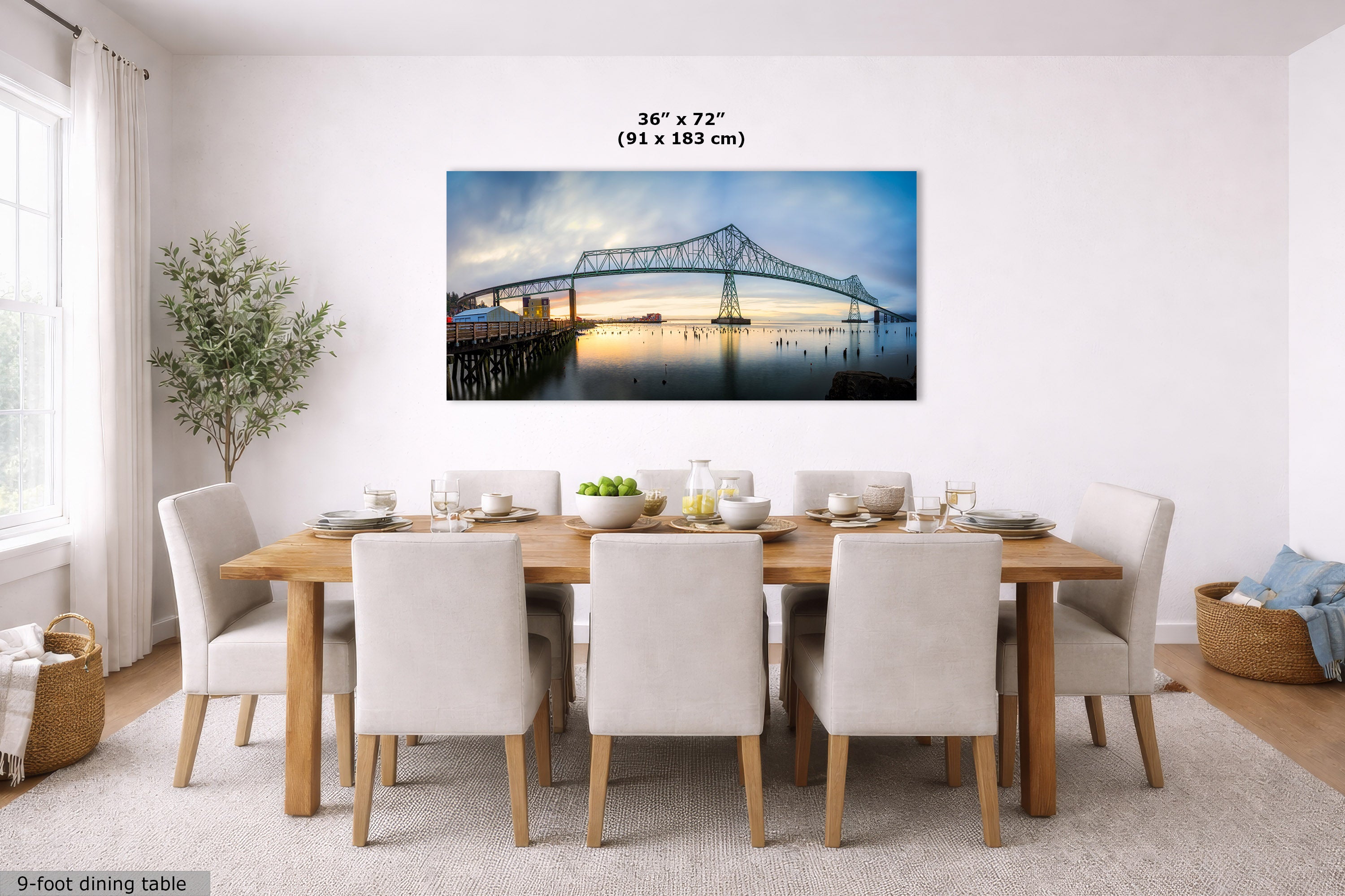 A framed wall art print of the Forth Bridge in Edinburgh, Scotland, displayed in a modern dining room setting above a wooden dining table and chairs. The print features a blue and white bridge over water at sunset, with dimensions '36" x 72" (91 x 183 cm)' printed above it.