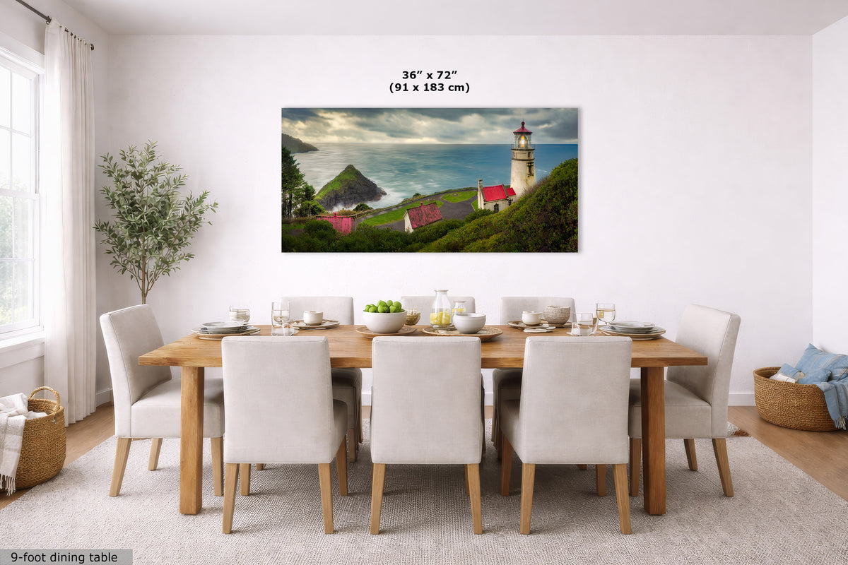 A framed wall art print showing a coastal lighthouse scene with green hills, red-roofed houses, and blue water, displayed above a dining table in a bright modern room. Text at the top reads 36 x 72 in (91 x 183 cm).