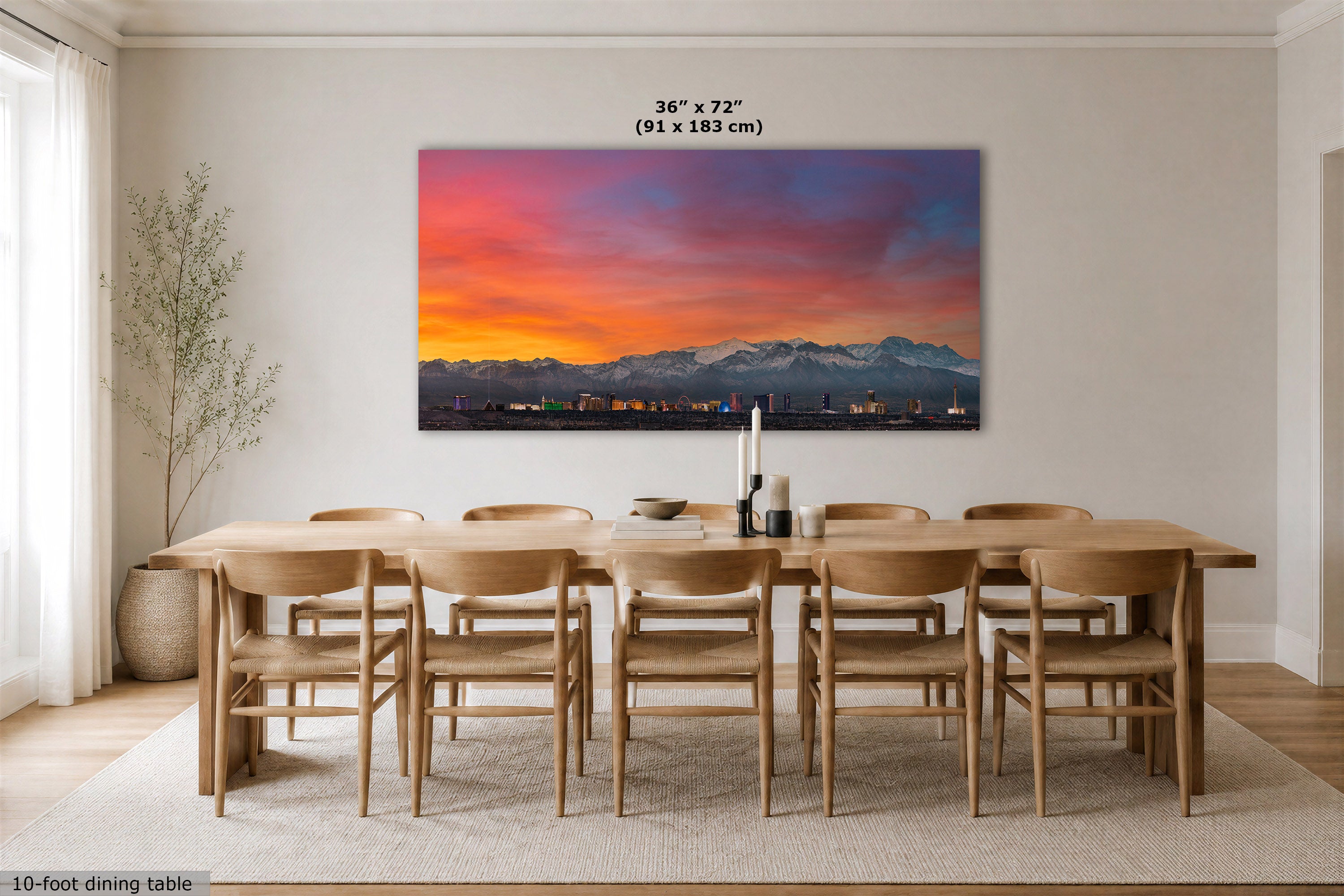 A large rectangular wall art print showing a colorful mountain sunset hangs above a wooden dining table and chairs in a bright modern dining room. The print includes size text reading 36 x 72 in (91 x 183 cm).