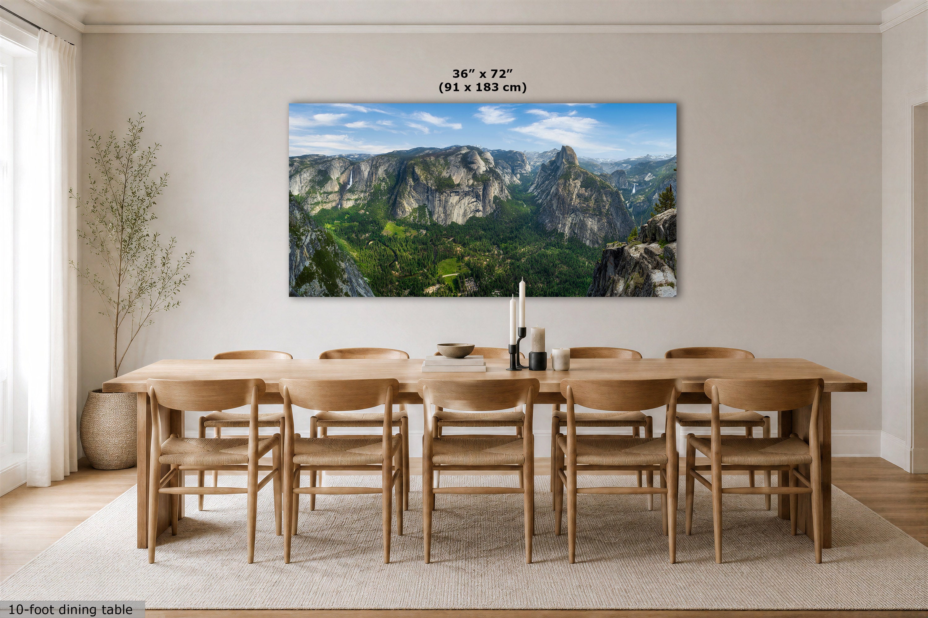 A large rectangular wall art print showing a mountain valley landscape hangs above a wooden dining table and chairs in a bright dining room. The print includes a size label reading 36 x 72 inches (91 x 183 cm).
