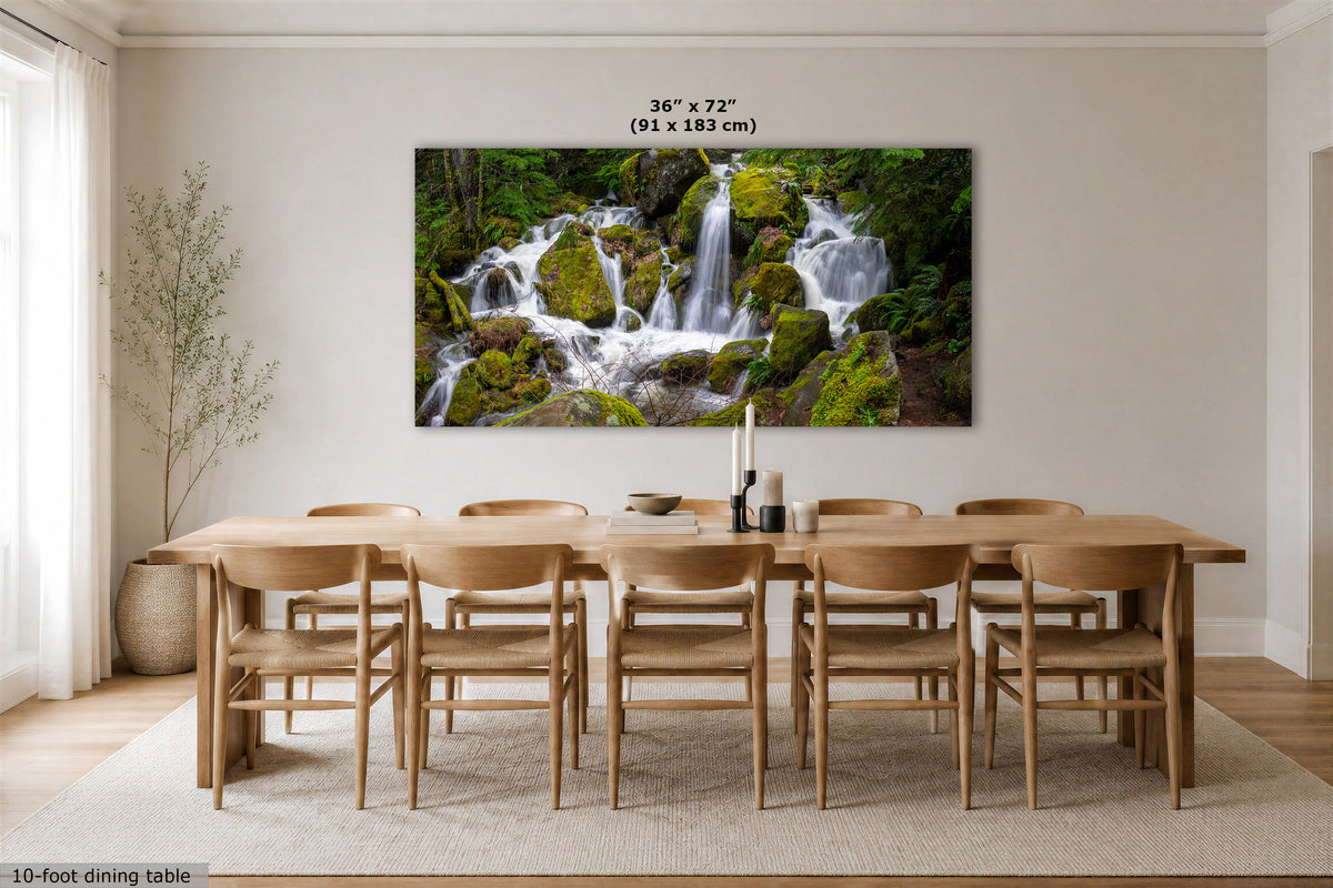 A large rectangular wall art print showing a lush waterfall scene with mossy rocks, displayed above a wooden dining table in a bright, modern dining room. The print includes size text reading 36 x 72" (91 x 183 cm) at the top.