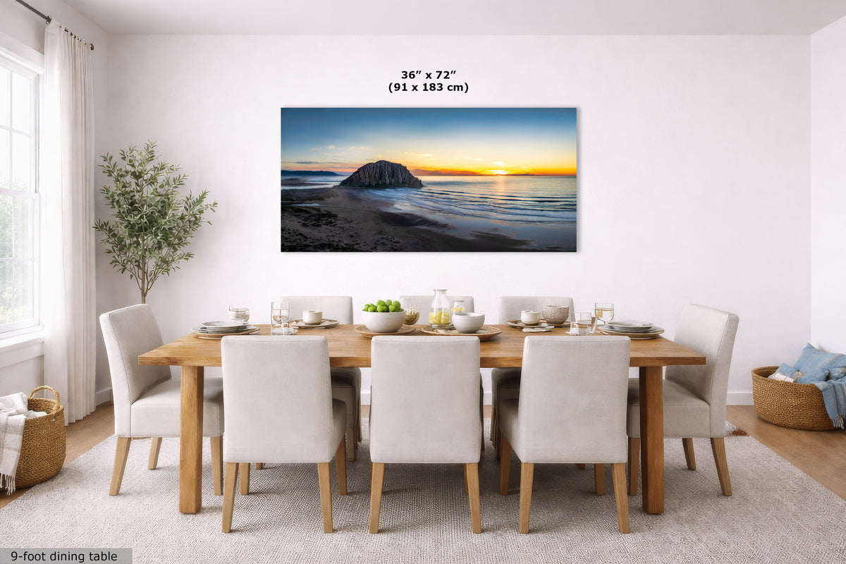 A wall art print showing a beach sunset with a rock formation is displayed above a dining table in a bright, modern dining room. The print has dimensions labeled as 36 x 72 inches (91 x 183 cm) above it.