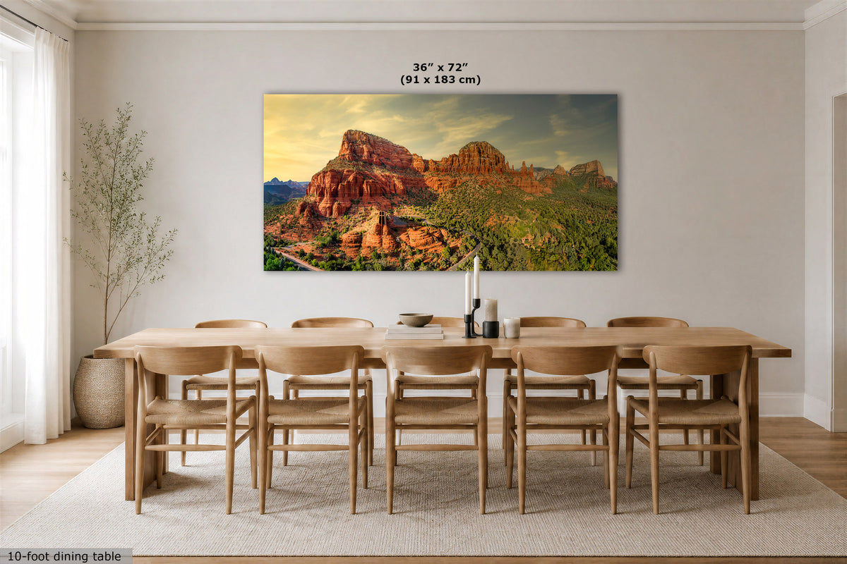 A large rectangular wall art print showing a desert rock landscape at sunset, displayed above a wooden dining table and chairs in a bright modern dining room. Text above the print reads 36 x 72" (91 x 183 cm).
