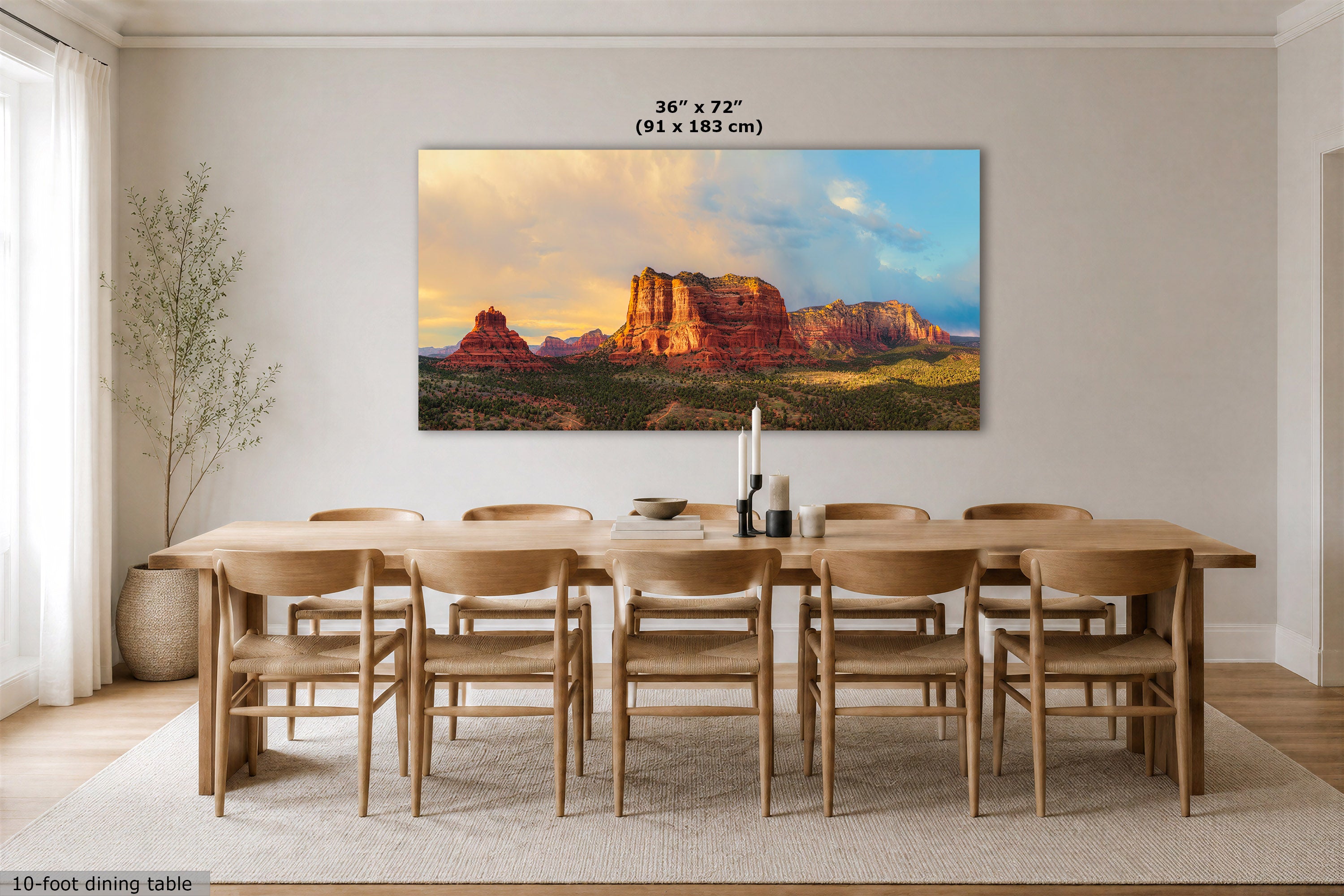 A large rectangular wall art print showing a desert rock landscape at sunset, displayed above a wooden dining table and chairs in a bright modern dining room. The print includes size text reading 36 x 72 in (91 x 183 cm).
