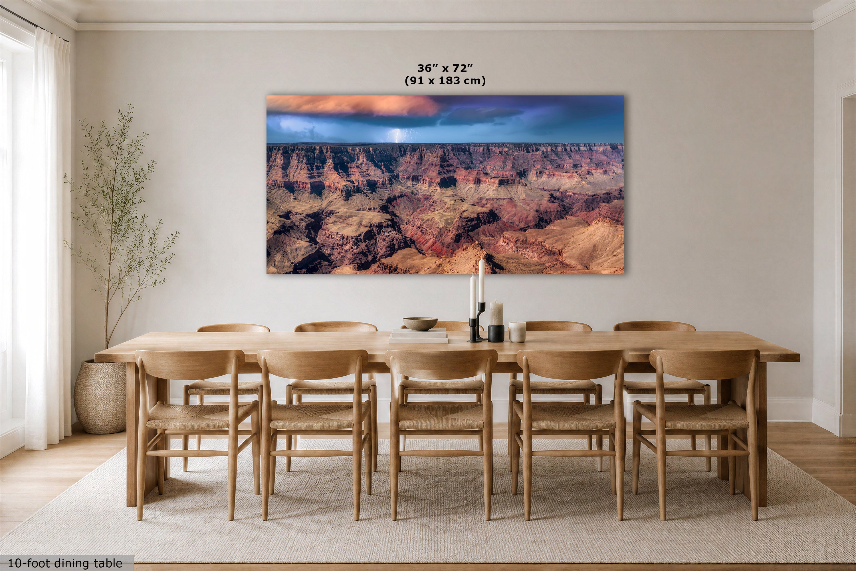 A large rectangular wall art print showing a canyon landscape with a glowing sun, displayed above a wooden dining table and chairs in a bright dining room. White text at the top reads 36 x 72" (91 x 183 cm).