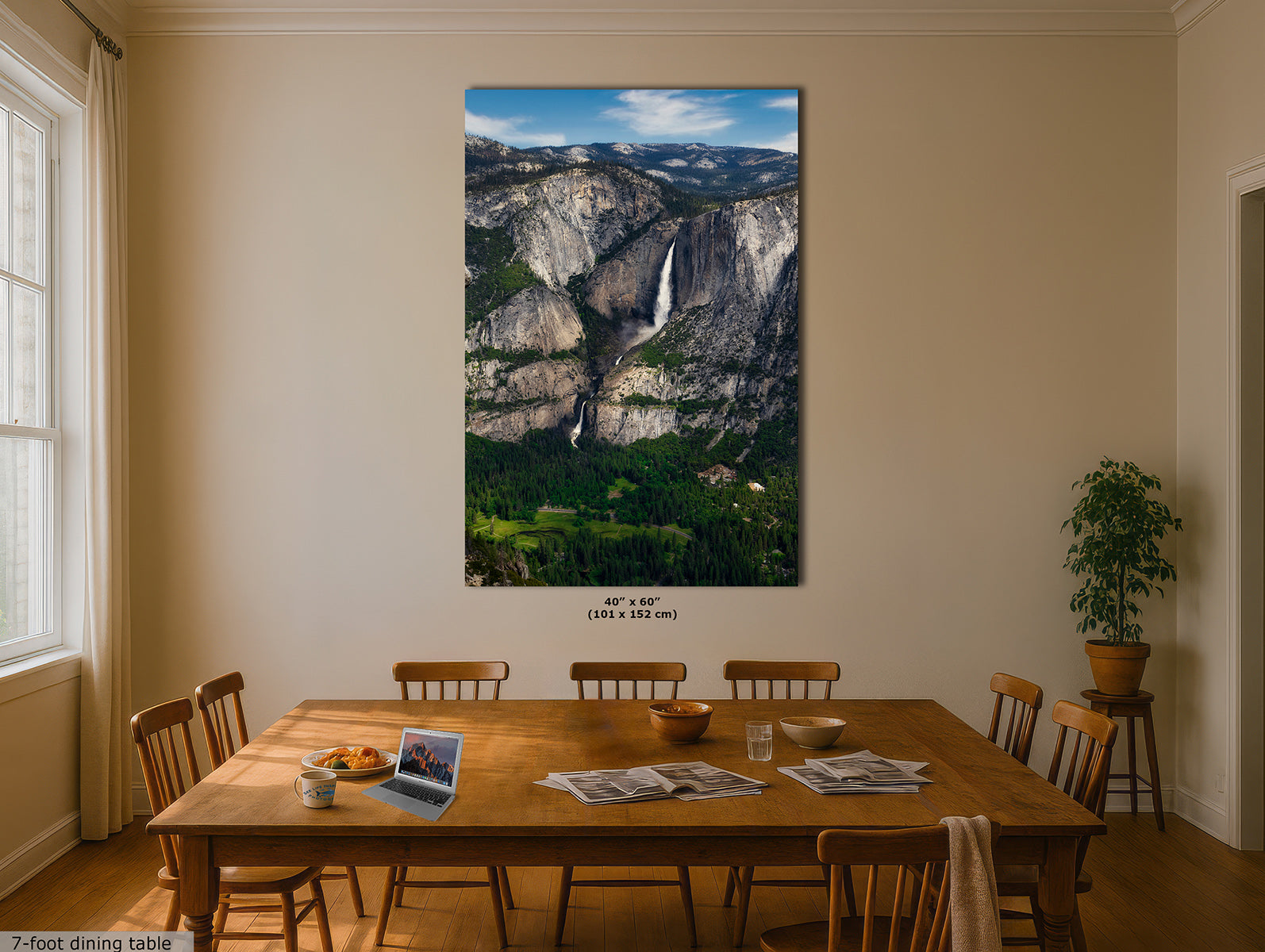 A large vertical print of Yosemite Falls hanging on a beige dining room wall above a wooden table with chairs. The print shows the waterfall cascading down a sheer cliff into a lush green valley under a blue sky.