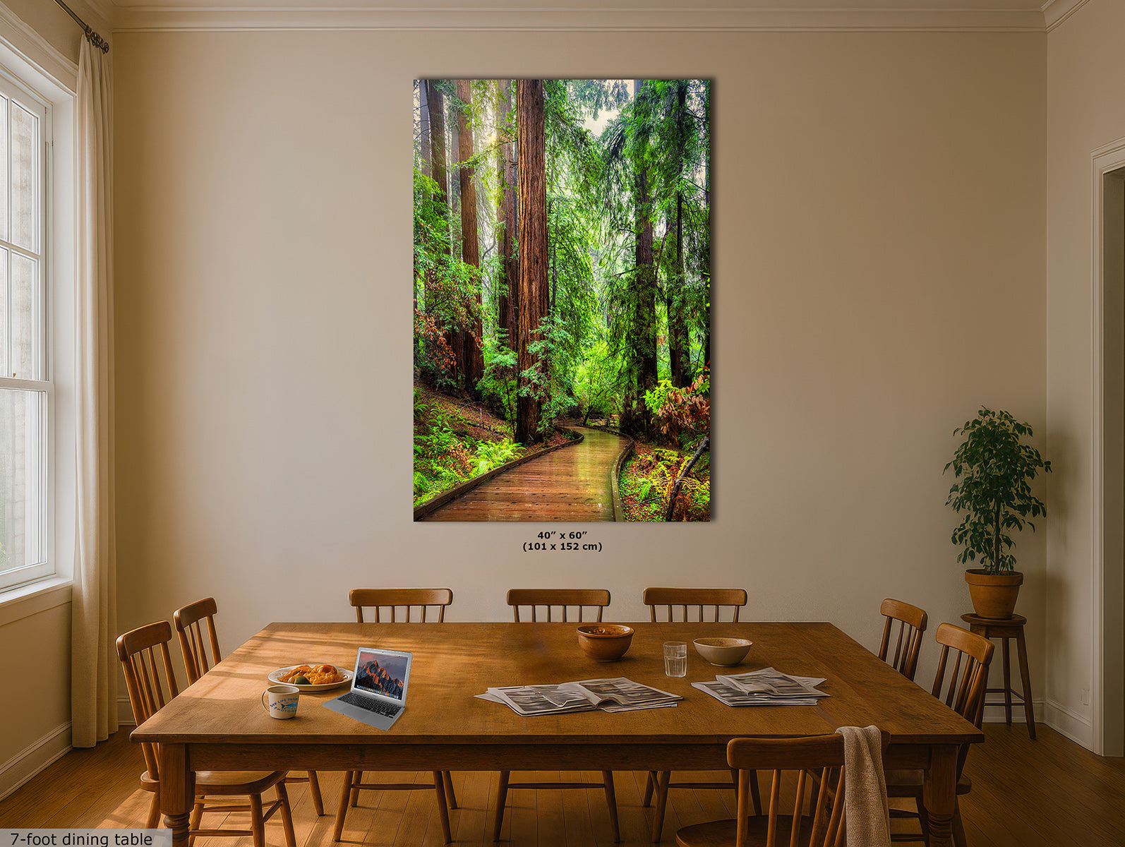 A vertical canvas wall art print depicting a lush green Redwood forest path with tall trees, displayed on a beige wall above a wooden dining table in a dining room setting.