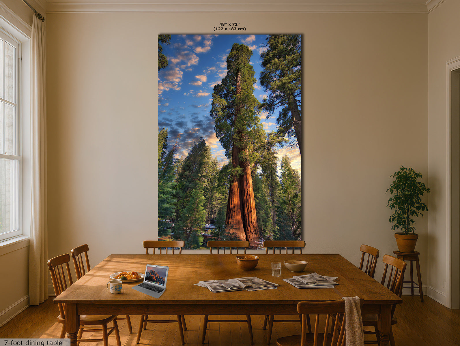 A large vertical wall art print depicting a giant sequoia tree in a forest under a blue sky, displayed on a beige dining room wall above a wooden dining table with chairs.