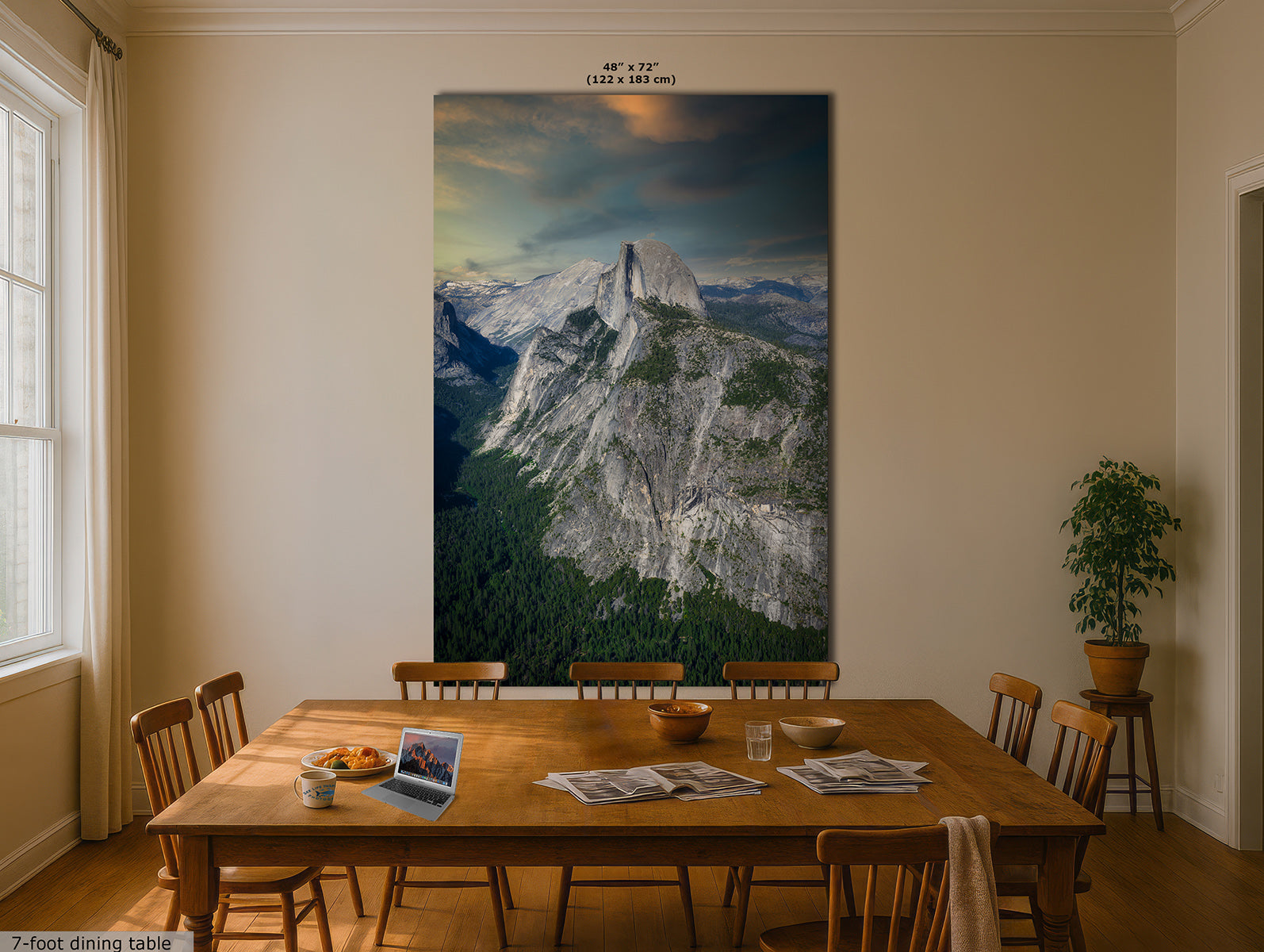 A large vertical wall art print of Half Dome in Yosemite, depicting a mountain landscape with a cloudy sky, displayed above a wooden dining table in a beige dining room. The print includes size text at the top and a small text note at the bottom left.