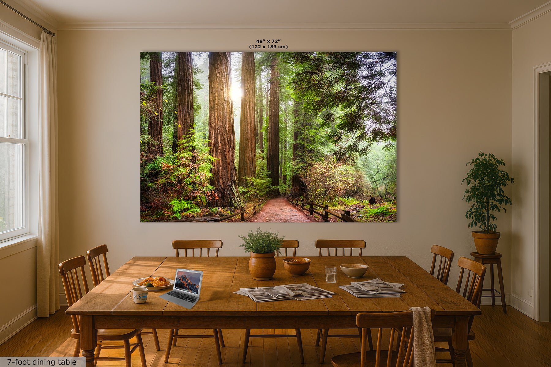 A large wall art print depicting a sunlit forest path with tall redwood trees and green foliage, displayed above a wooden dining table in a beige dining room.