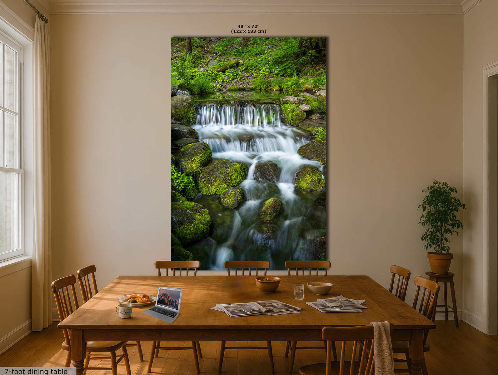 A large vertical wall art print showing a lush green forest waterfall cascading over mossy rocks, displayed in a dining room above a wooden table.