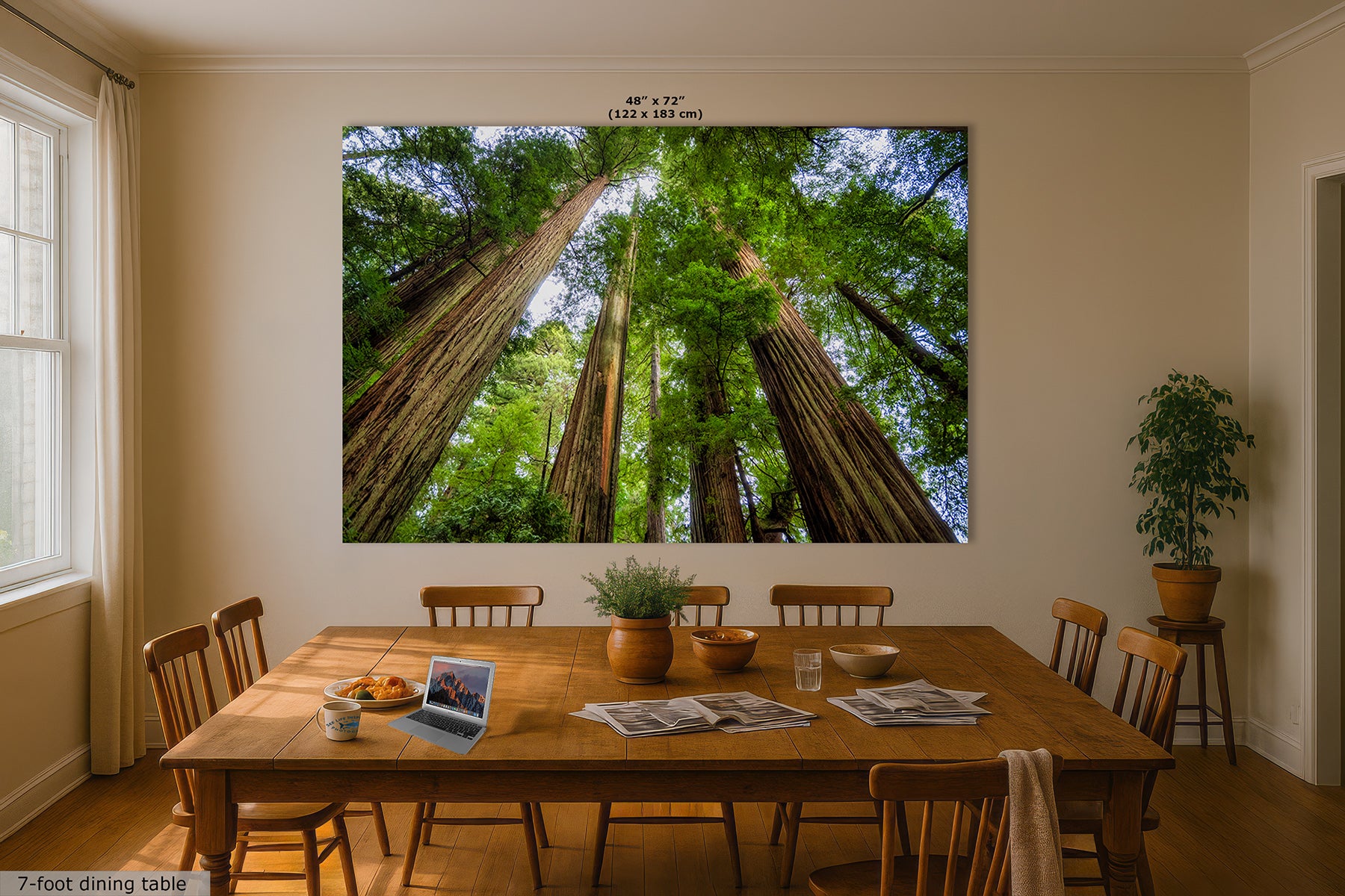 A large wall art print depicting a low-angle view of giant redwood trees is displayed on a beige wall in a dining room setting with a wooden dining table and chairs.