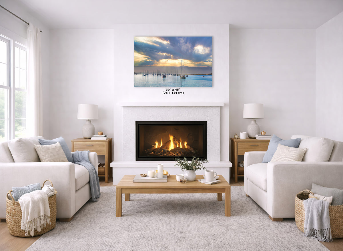 A wall art print depicting a sunset over a calm harbor with a dock, displayed above a fireplace in a bright, modern living room with white sofas and a wooden coffee table.