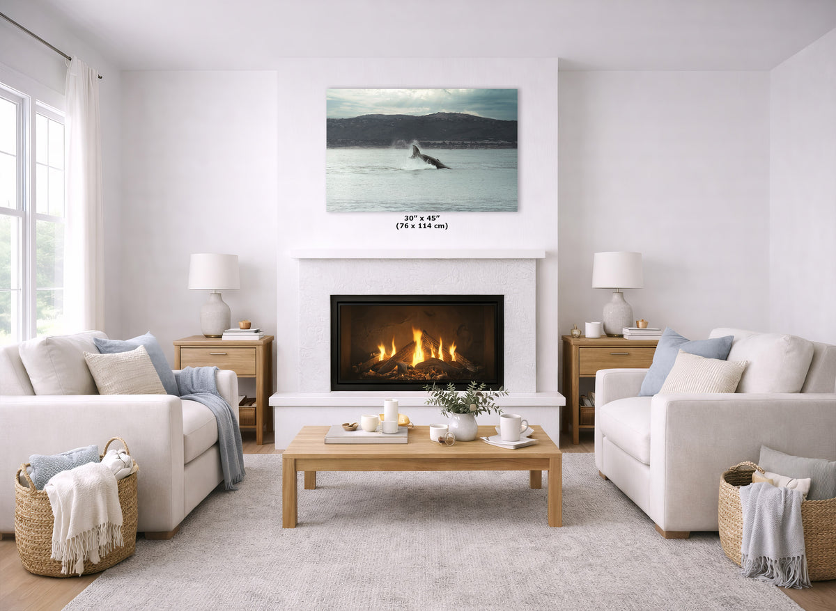 A wall art print depicting a whale in blue-gray water with dark mountains in the distance, displayed above a fireplace in a bright, modern living room with white sofas, a wooden coffee table, and a light rug.