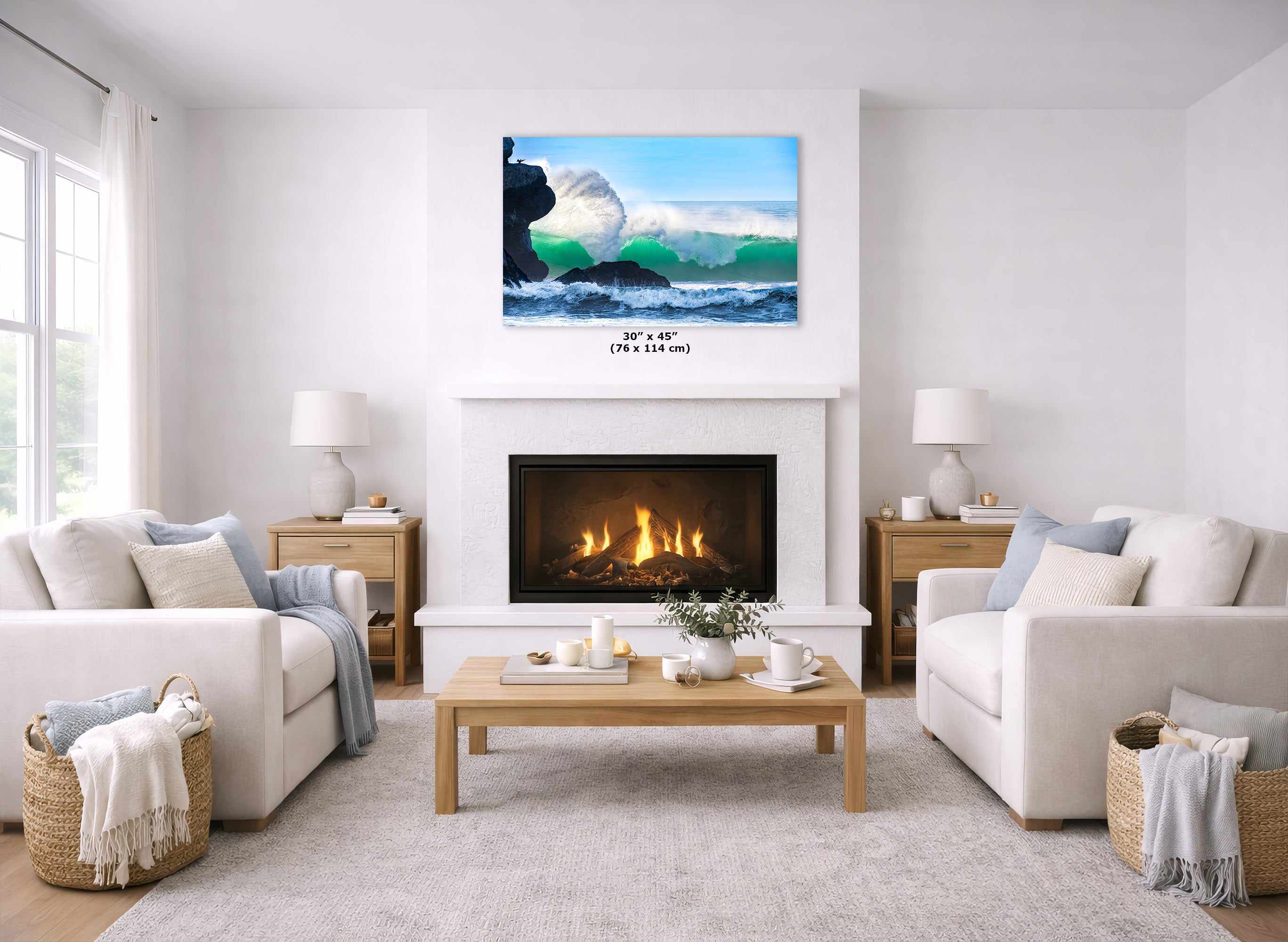 A landscape art print of ocean waves is displayed on the wall above a white fireplace in a bright, modern living room with two white sofas and a wooden coffee table.
