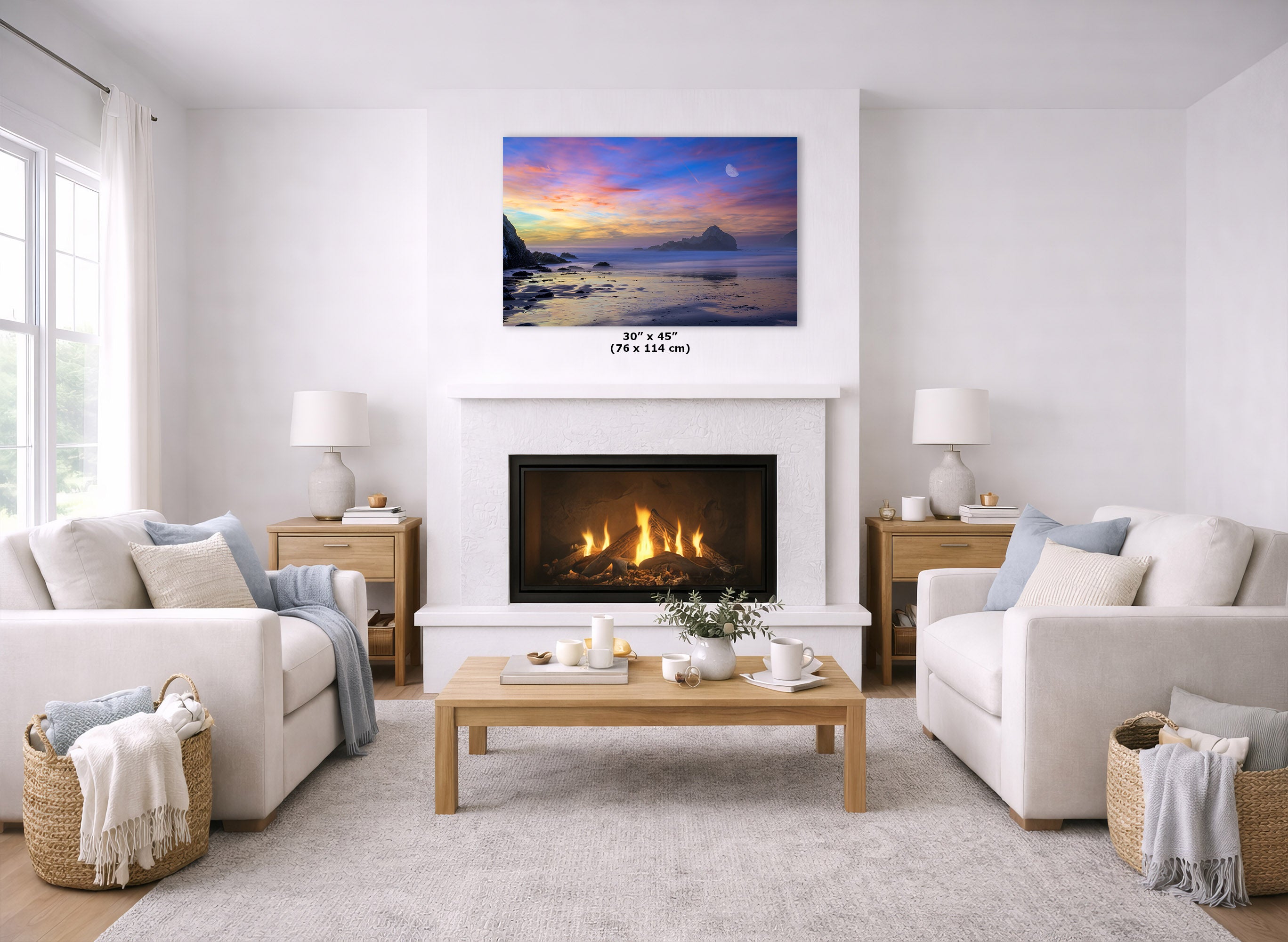 A landscape art print of a colorful sunset over water hangs above a white fireplace in a bright, modern living room with two white sofas and a wooden coffee table.