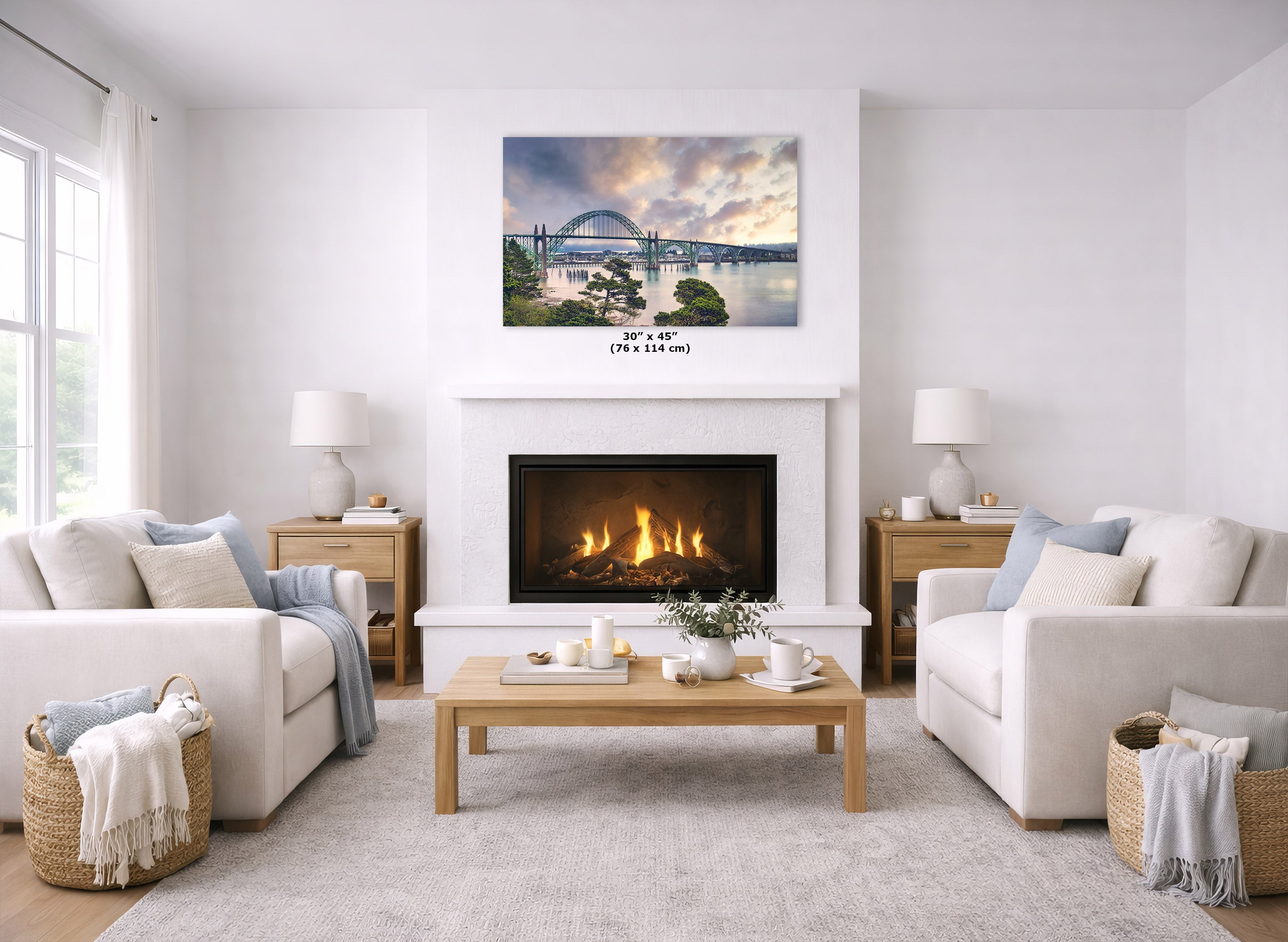 A landscape art print of a bridge over water hangs above a white fireplace in a bright, modern living room with two cream sofas, a wooden coffee table, and a light rug.