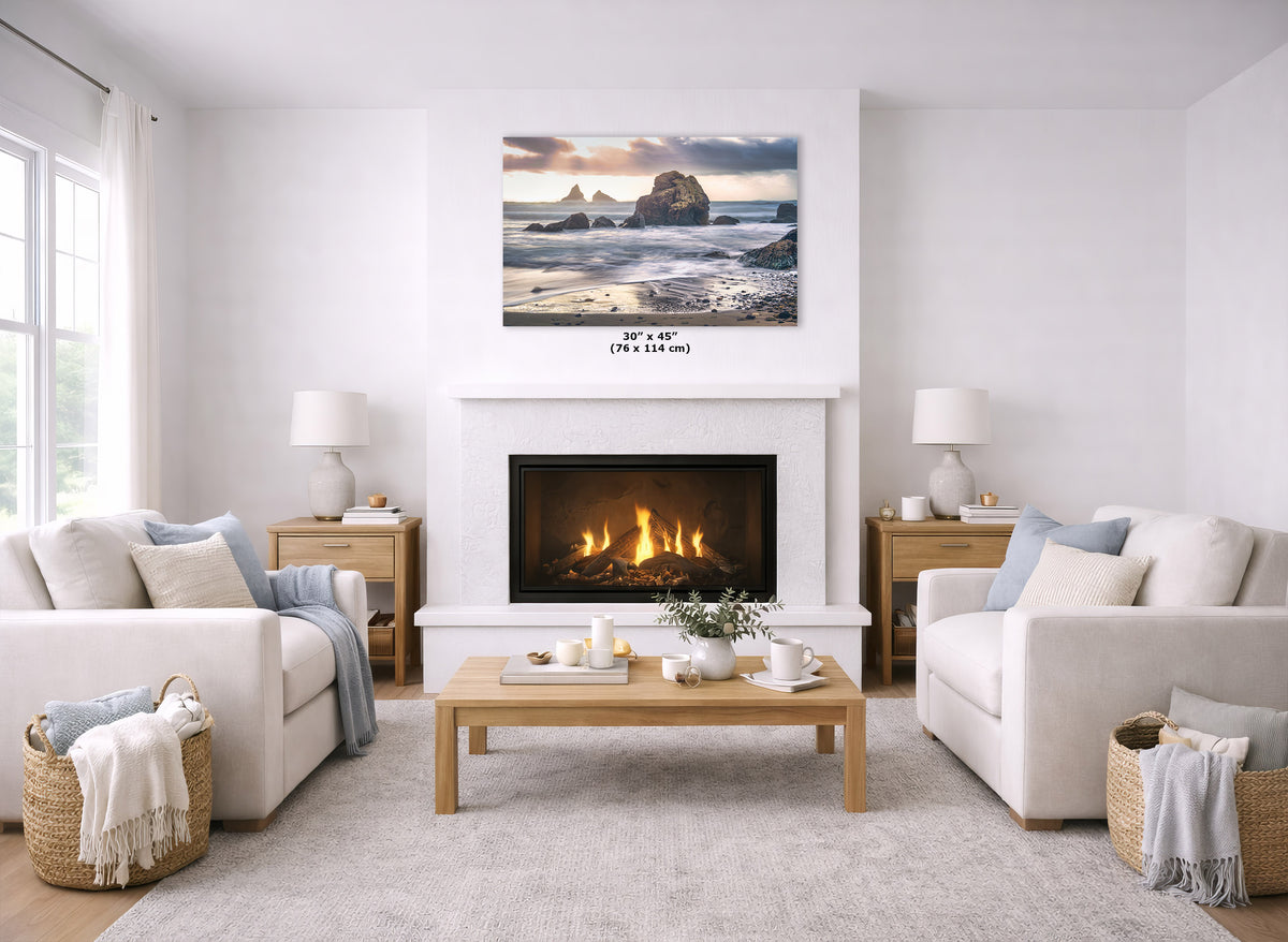 A coastal landscape wall art print hangs above a white fireplace in a bright, modern living room with two cream sofas, a wooden coffee table, and woven baskets.