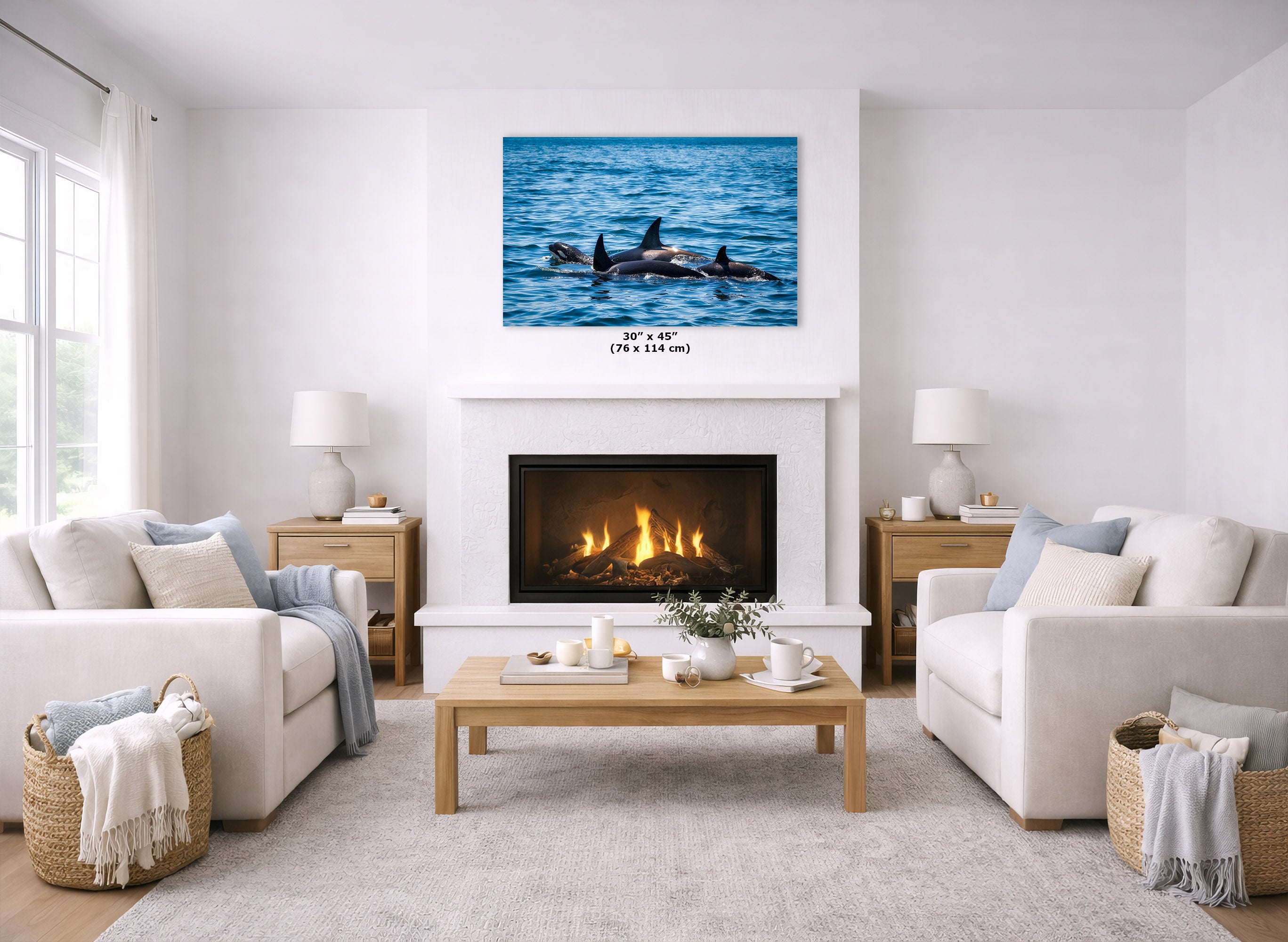 A wall art print showing blue ocean water with several orcas, displayed above a fireplace in a bright, modern living room with white sofas, a wooden coffee table, and woven baskets.