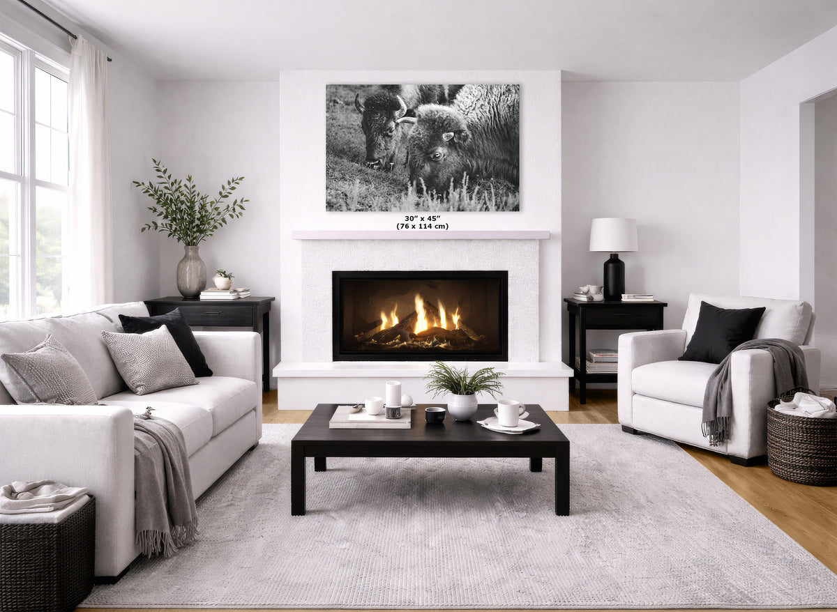 A black and white art print displayed in a modern living room setting above a white fireplace mantel, with a fire burning inside. The room features a white sofa, a white accent chair, a dark wood coffee table, and a light gray textured rug.