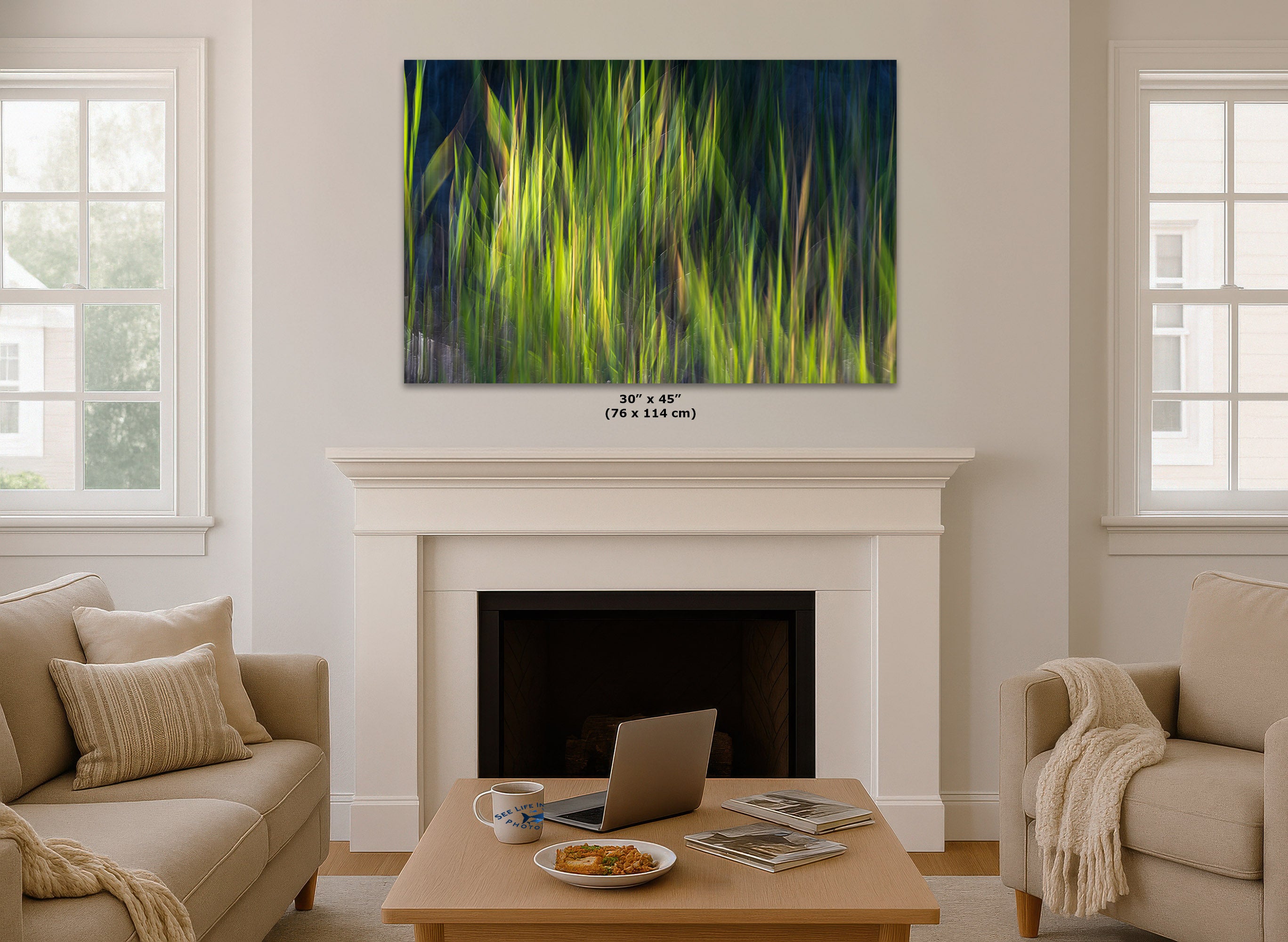 A framed abstract wall art print depicting vibrant green and yellow grasses against a dark blue background, displayed in a mockup living room above a white fireplace mantel.