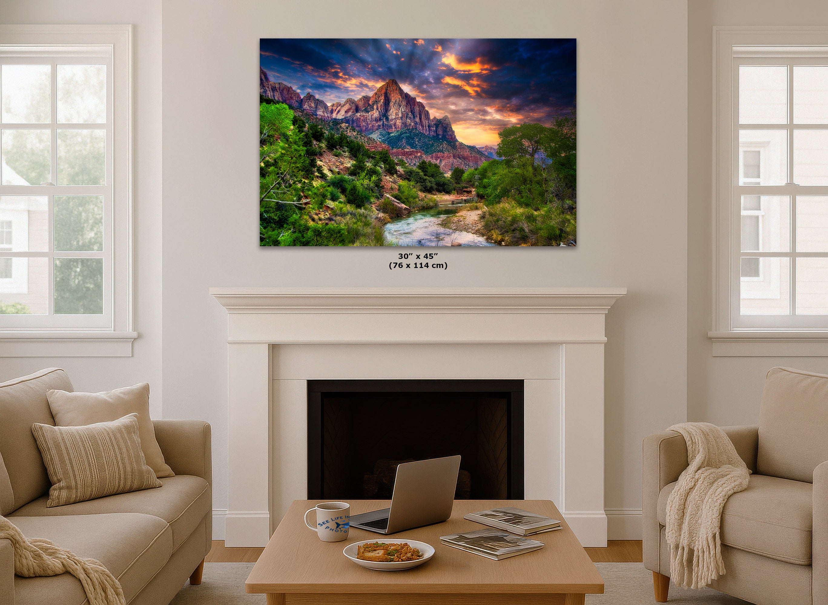 A wall art print depicting a colorful Zion mountain landscape with a river and dramatic sunset sky, displayed above a white fireplace mantel in a bright living room. Small text below the print reads 30 x 45 (76 x 114 m).