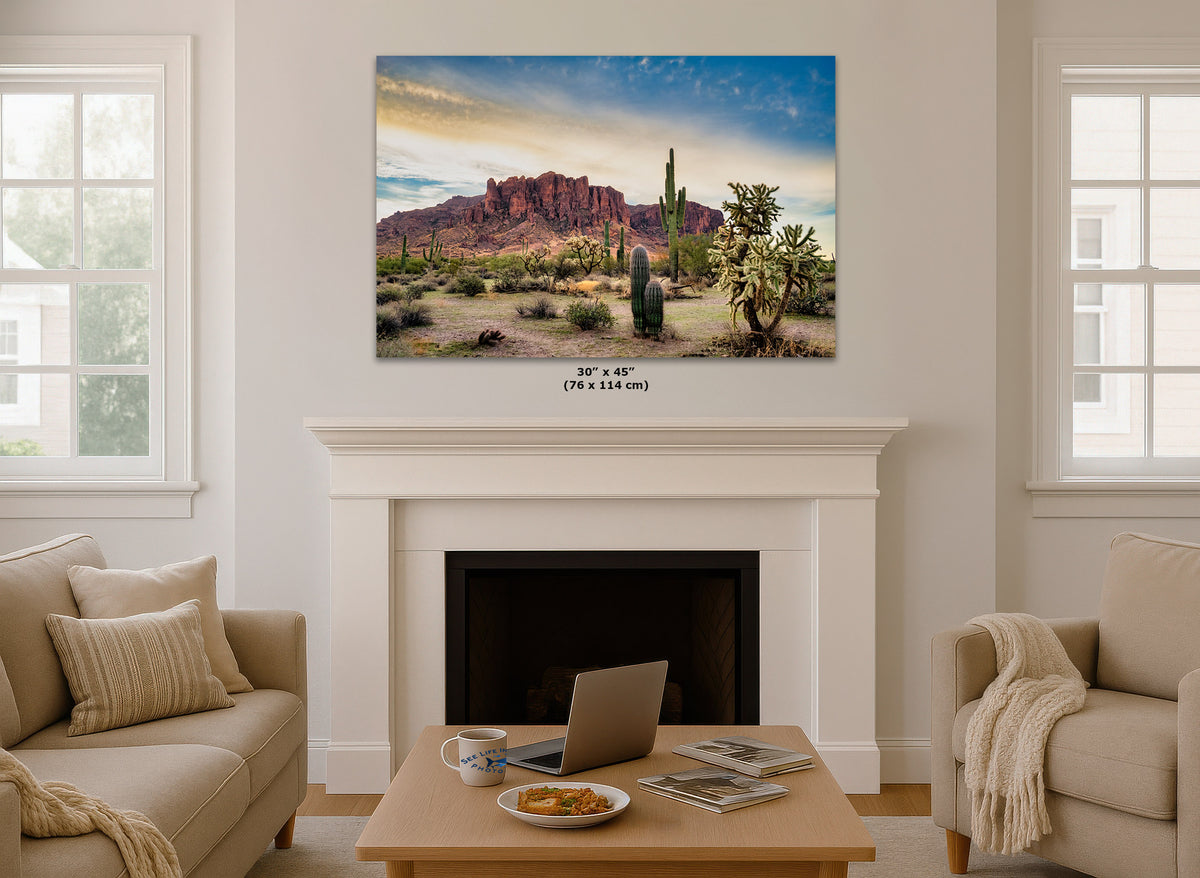A desert landscape wall art print hangs above a white fireplace mantel in a bright living room. The artwork shows red rock desert mountains, cacti, and a blue sky.