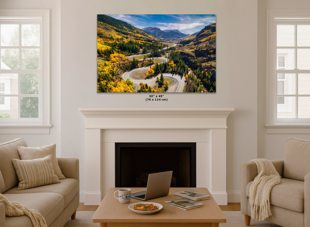 Living room with a large wall art print of Colorado's Million Dollar Highway with yellow aspen trees hanging above a fireplace.