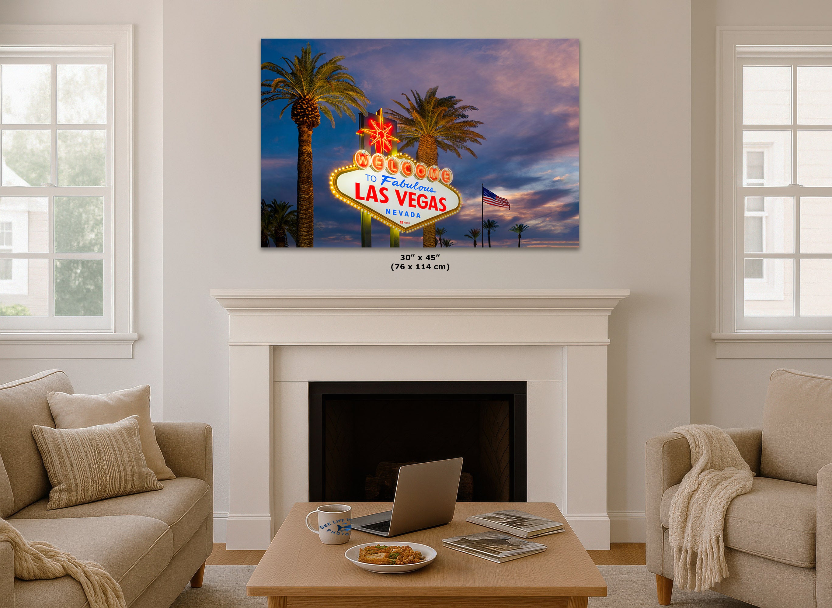 A wall art print showing the Las Vegas sign at dusk, displayed above a white fireplace in a staged living room with beige sofas and a coffee table.