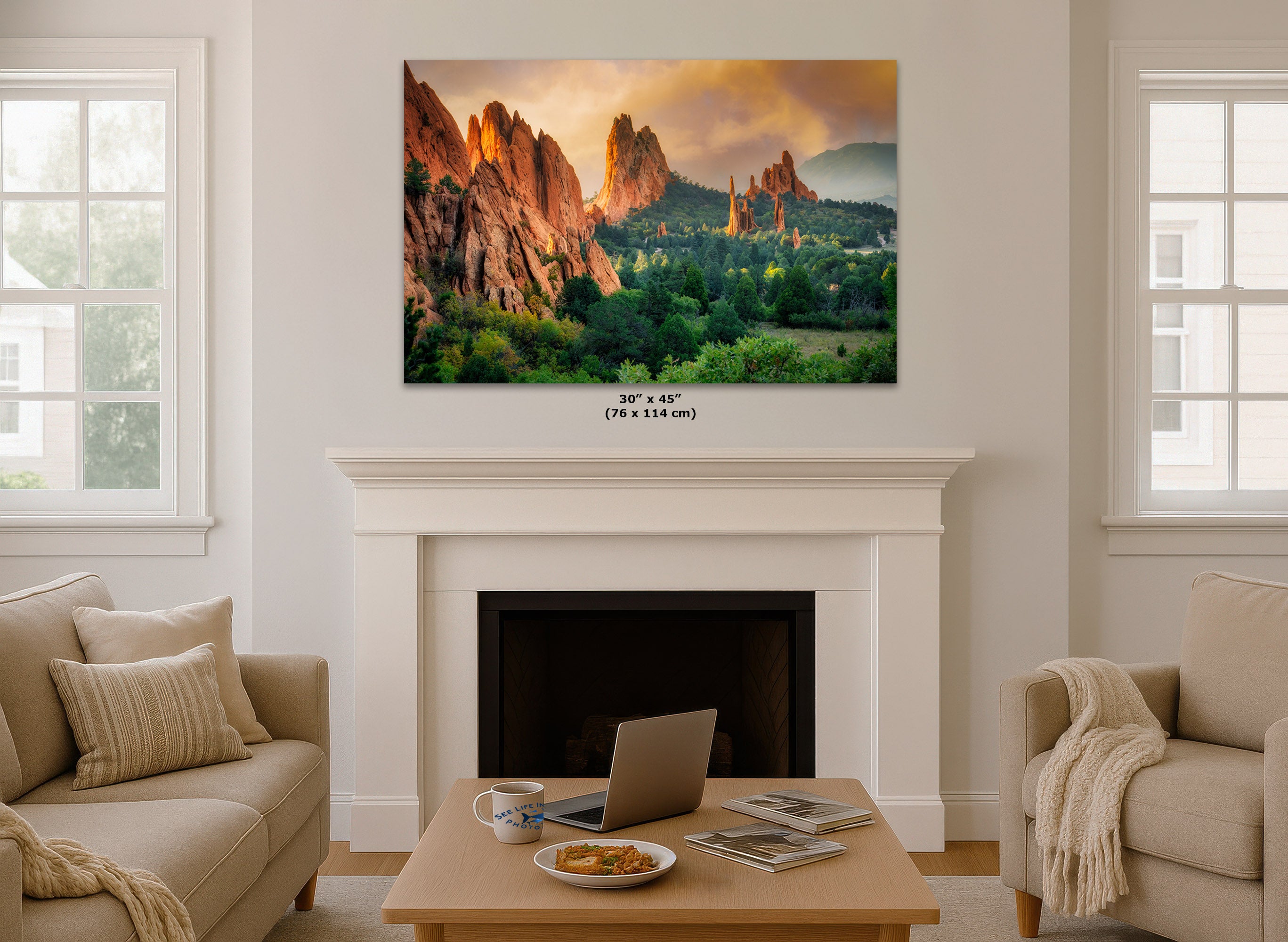 A wall art print showing a colorful landscape of red rock spires and green trees, displayed above a white fireplace mantel in a bright living room. Small text below the print reads 30" x 45" (76 x 114 cm).