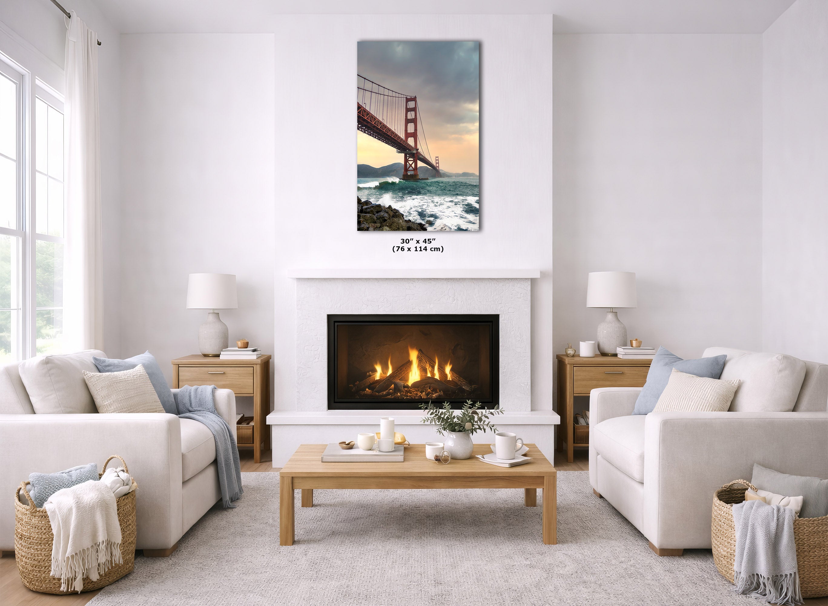 A framed wall art print of the Golden Gate Bridge over ocean waves hangs above a fireplace in a bright, modern living room with white sofas, a wooden coffee table, and neutral decor.