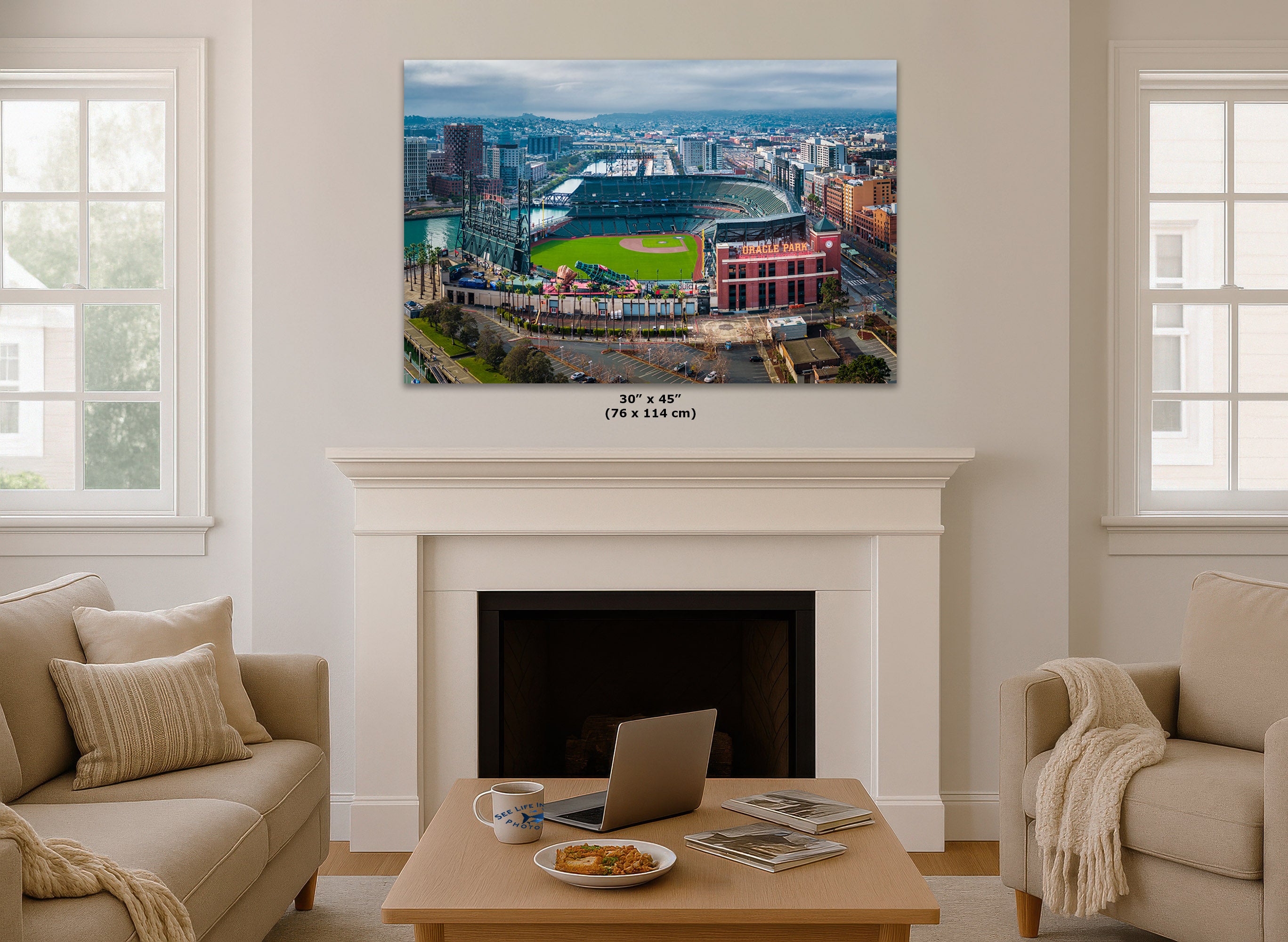 A Oracle Park Stadium wall art print showing an aerial view of a baseball stadium and surrounding cityscape, displayed above a white fireplace mantel in a bright living room. The print includes size text reading 30 x 45 inches (76 x 114 cm).