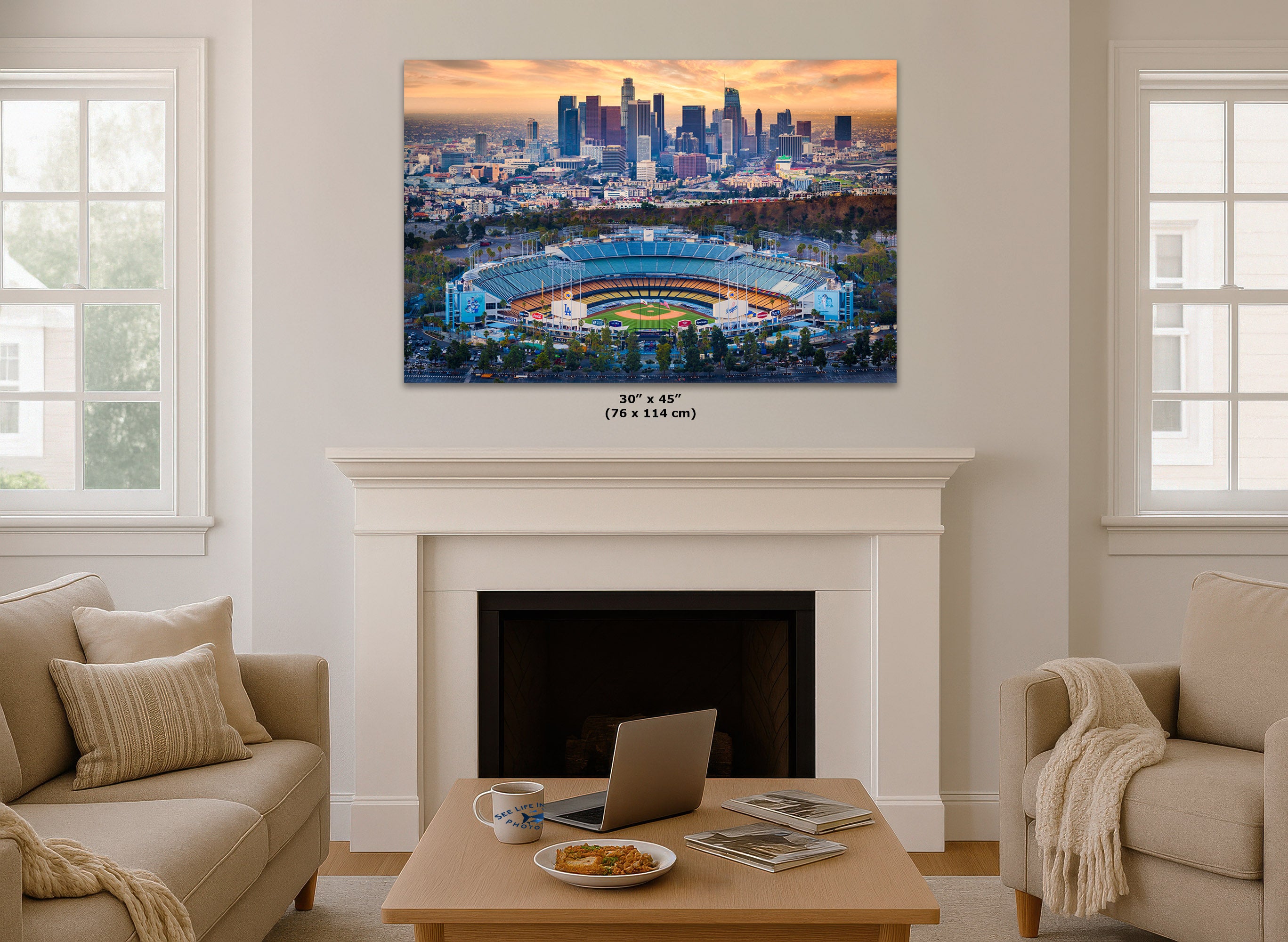 A Dodger Stadium wall art print showing a city skyline and a stadium at sunset, displayed above a white fireplace in a bright living room. Small text below the print reads 30" x 45" (76 x 114 cm).