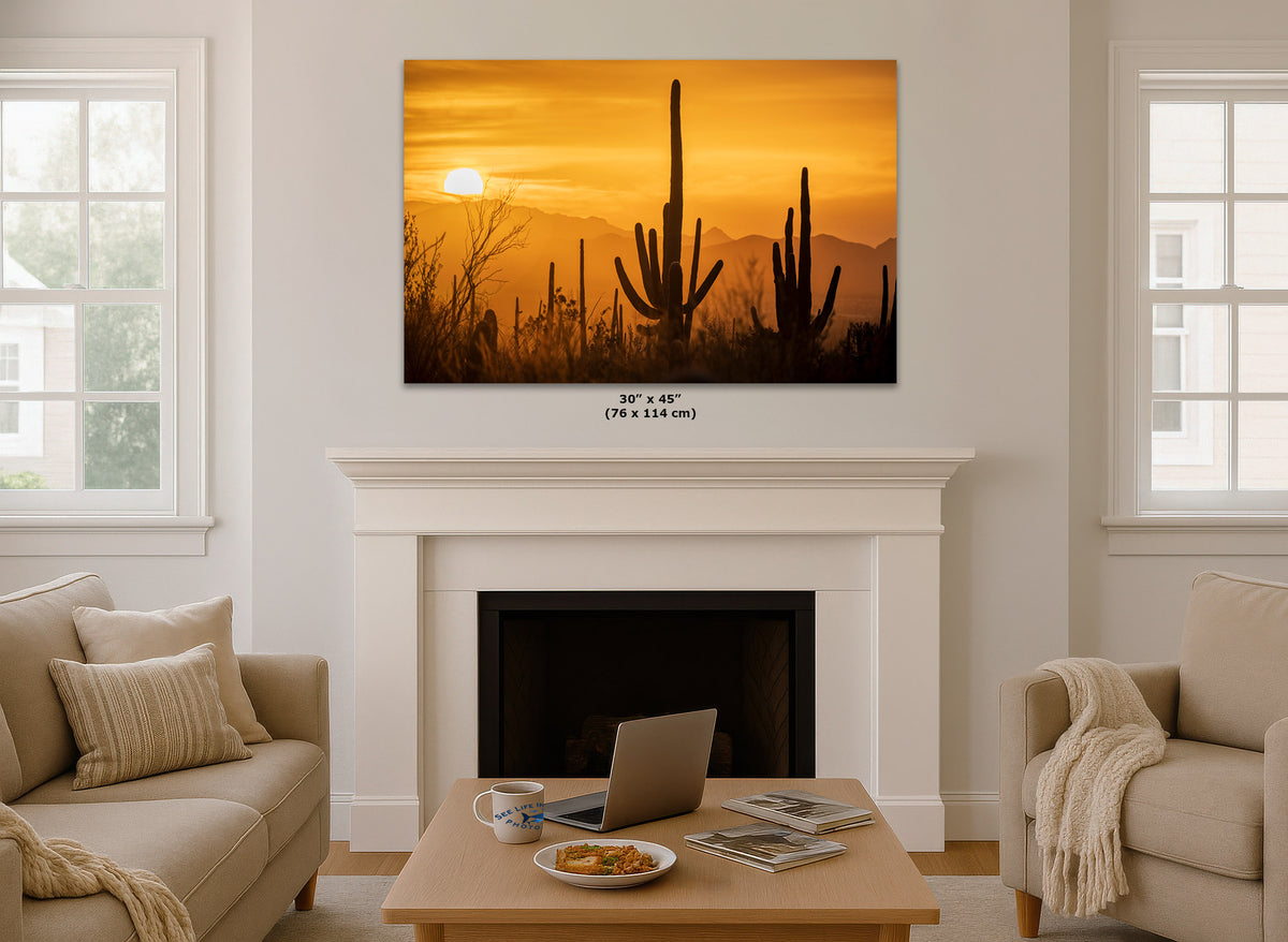 A wall art print showing a desert sunset with cacti and mountains, displayed above a white fireplace mantel in a bright living room. Small text below the print reads 30 x 45 in (76 x 114 cm).
