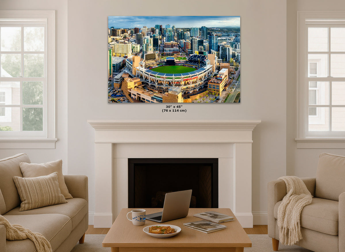 A San Diego Padres Stadium art print showing an aerial view of Petco Park stadium and the surrounding San Diego city skyline in California, displayed above a white fireplace mantel in a bright living room. Small text below the print reads 30" x 45" (76 x 114 cm).
