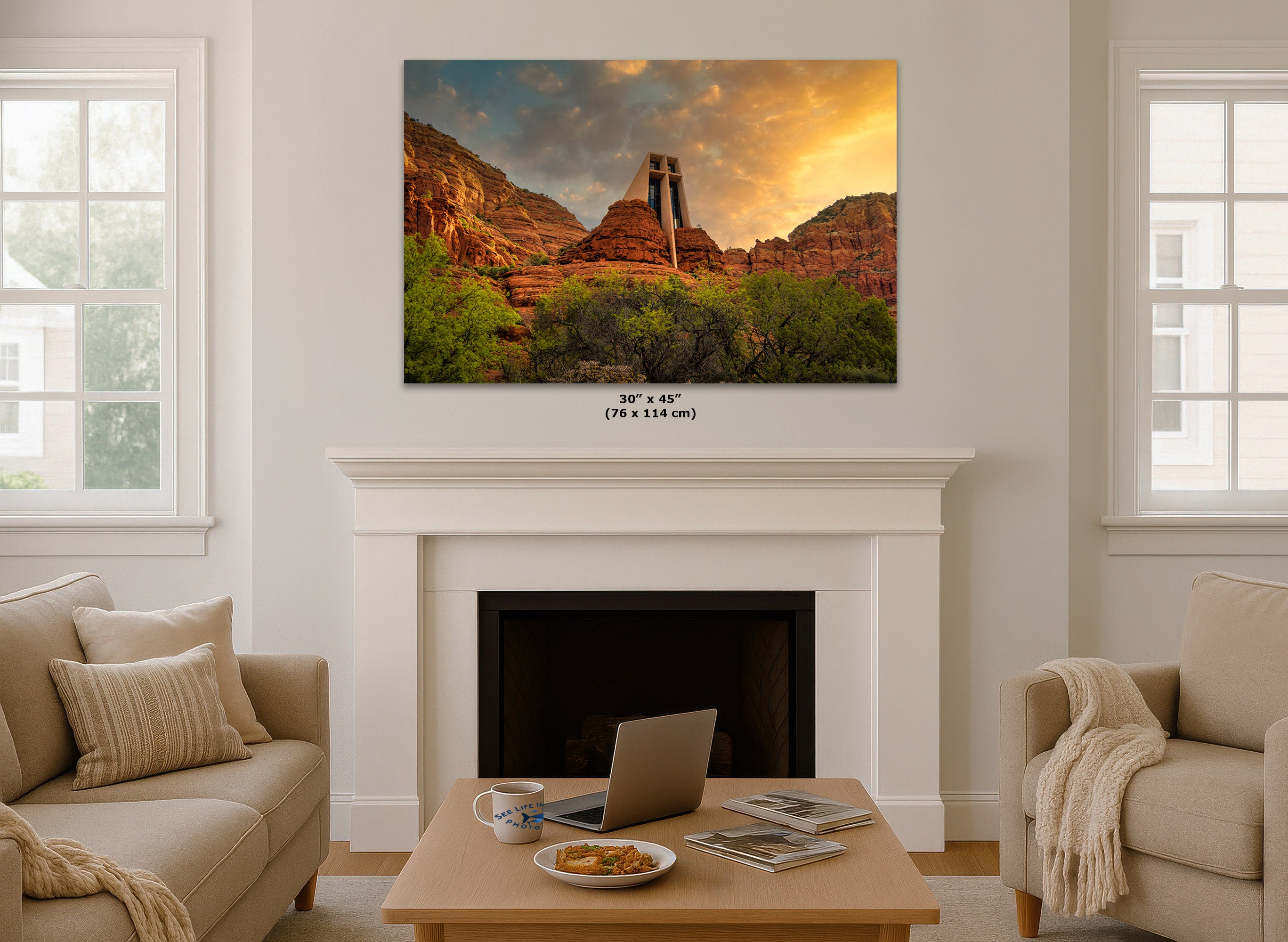 A wall art print showing a desert canyon landscape at sunset, displayed above a white fireplace mantel in a bright living room. Small text below the print reads 30 x 45 in (76 x 114 cm).