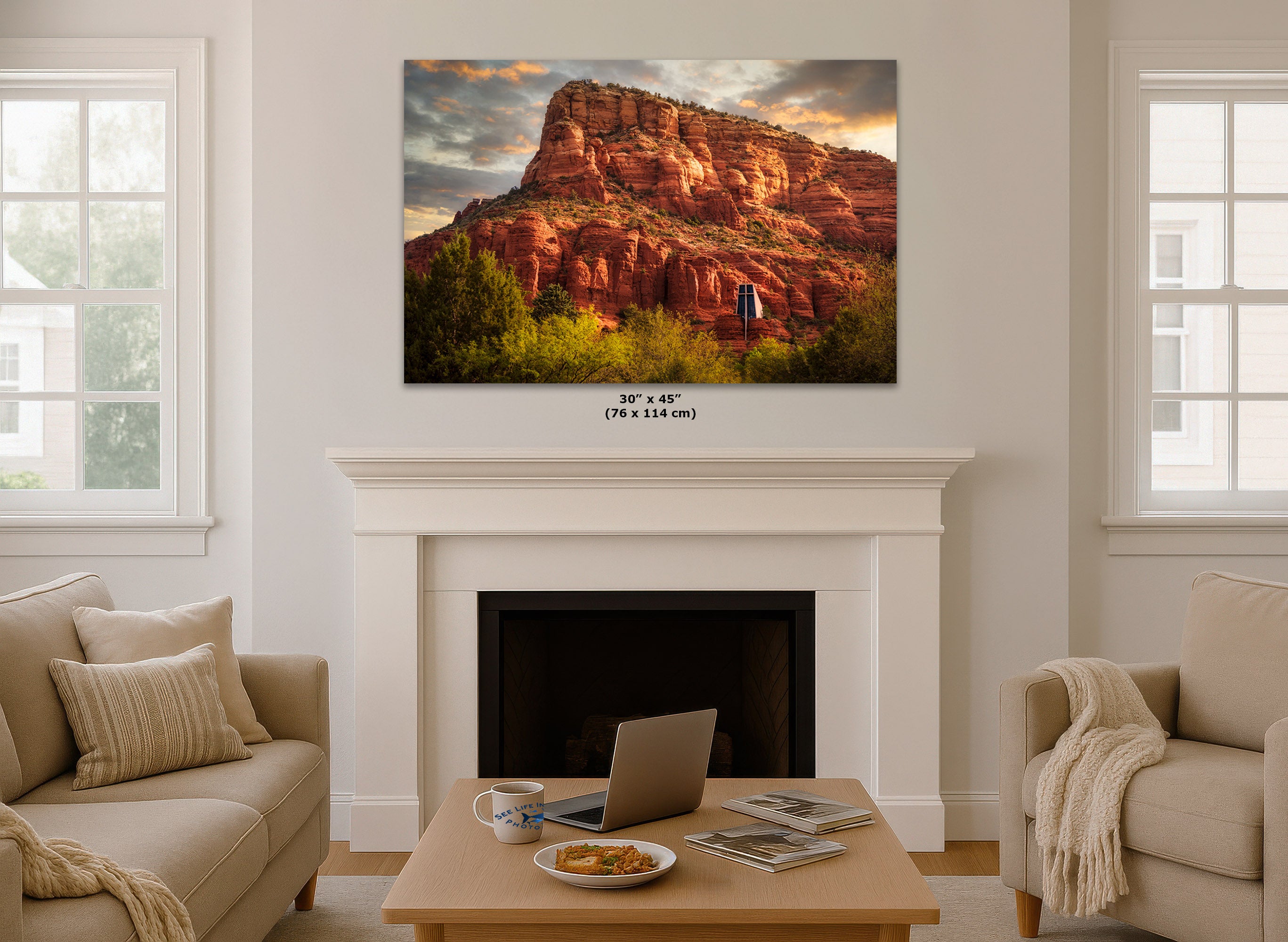 A wall art print depicting a red rock desert canyon at sunset, displayed above a white fireplace mantel in a bright living room. The print includes size text below it reading 30 x 45 in (76 x 114 cm).
