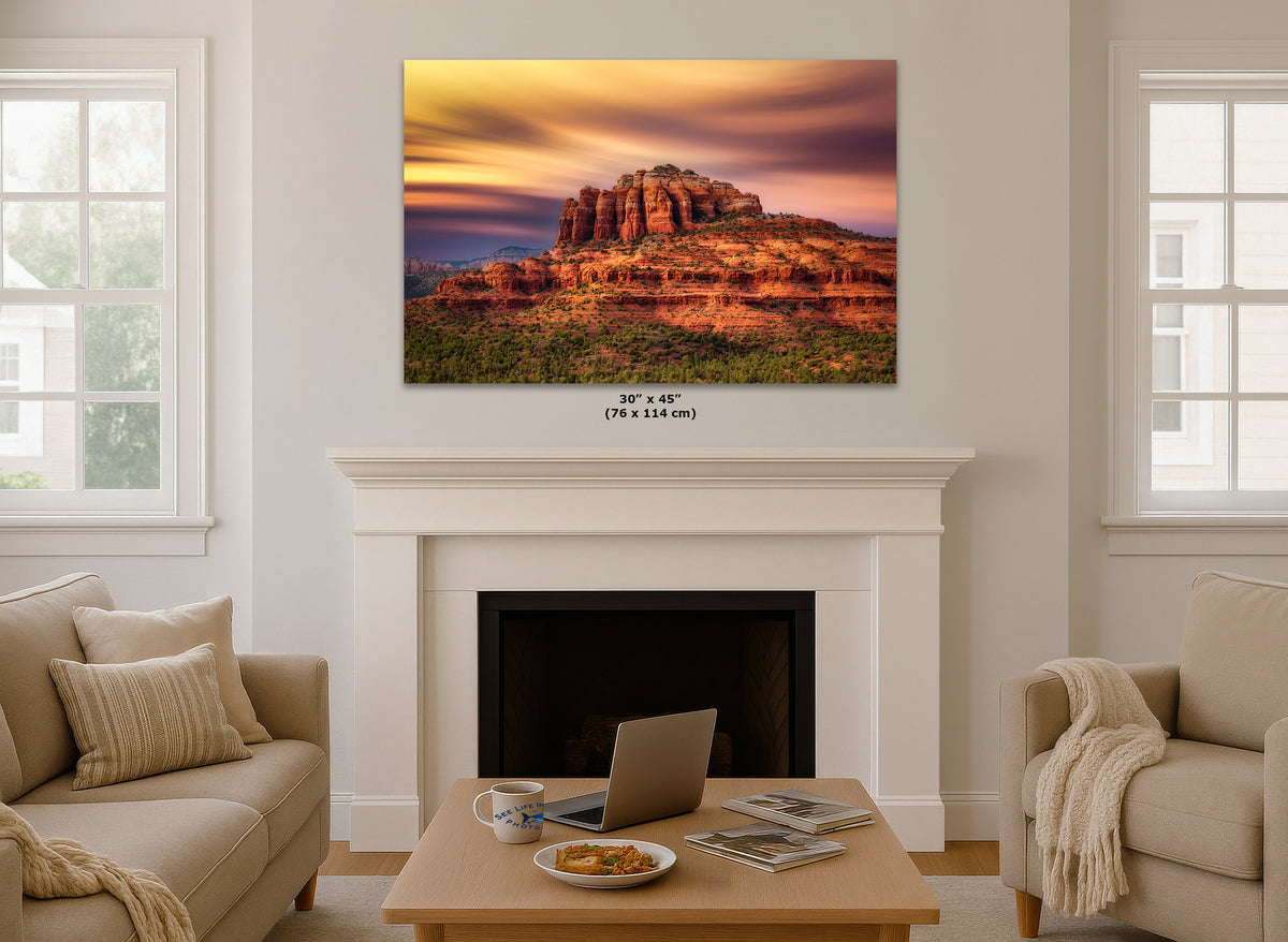 A wall art print showing a desert rock formation at sunset, displayed above a white fireplace mantel in a bright living room. Small text below the print reads 30 x 45 (76 x 114 cm).