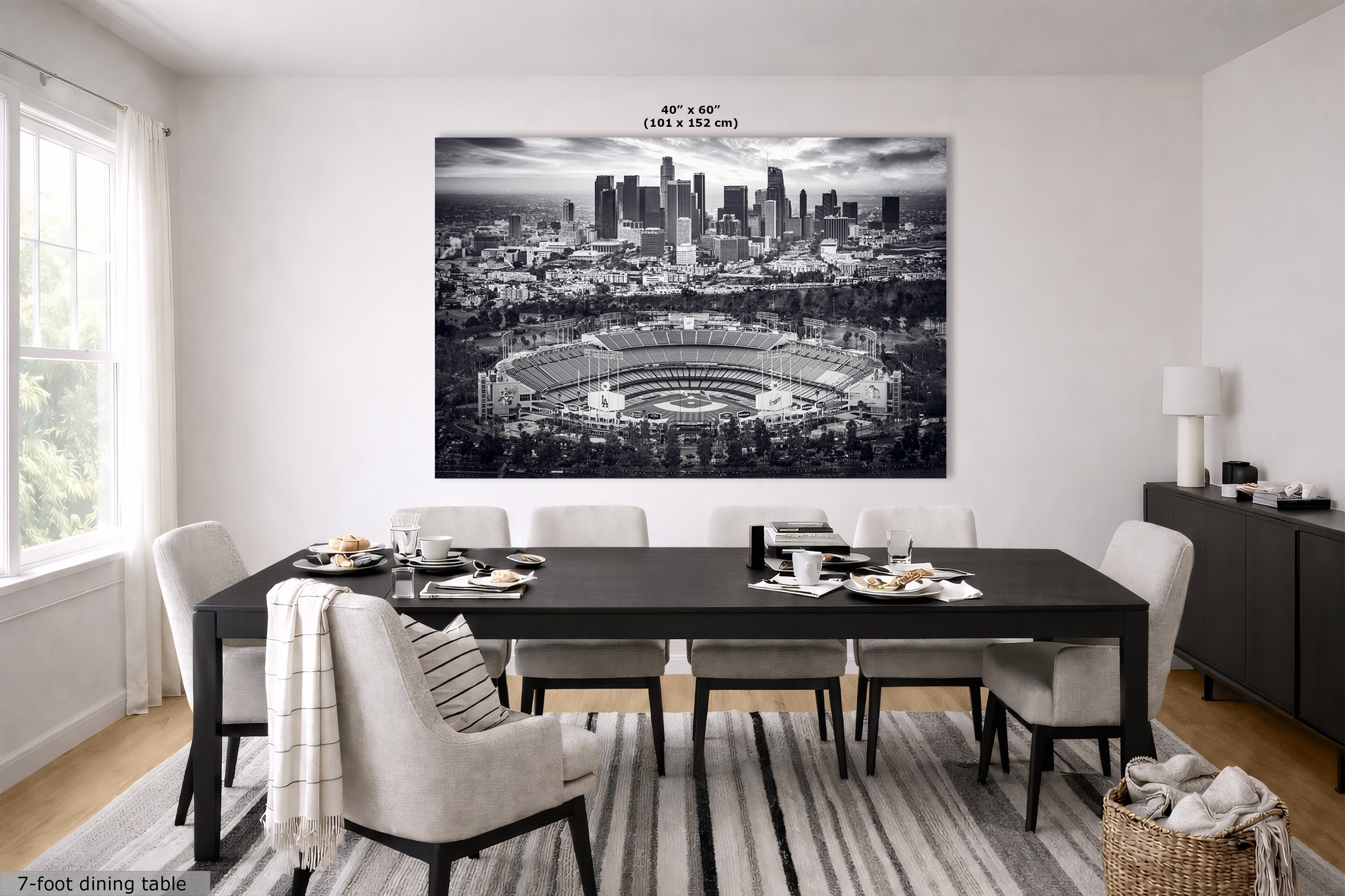 A large black and white wall art print of a stadium and city skyline hangs above a dark dining table in a modern dining room. The print includes size text reading 40 in x 60 in.