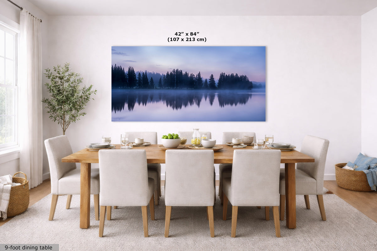 A large wall art print showing a misty forest lake at dusk, displayed above a dining table in a bright modern dining room. The print includes size text reading 42 x 84 inches (107 x 213 cm).