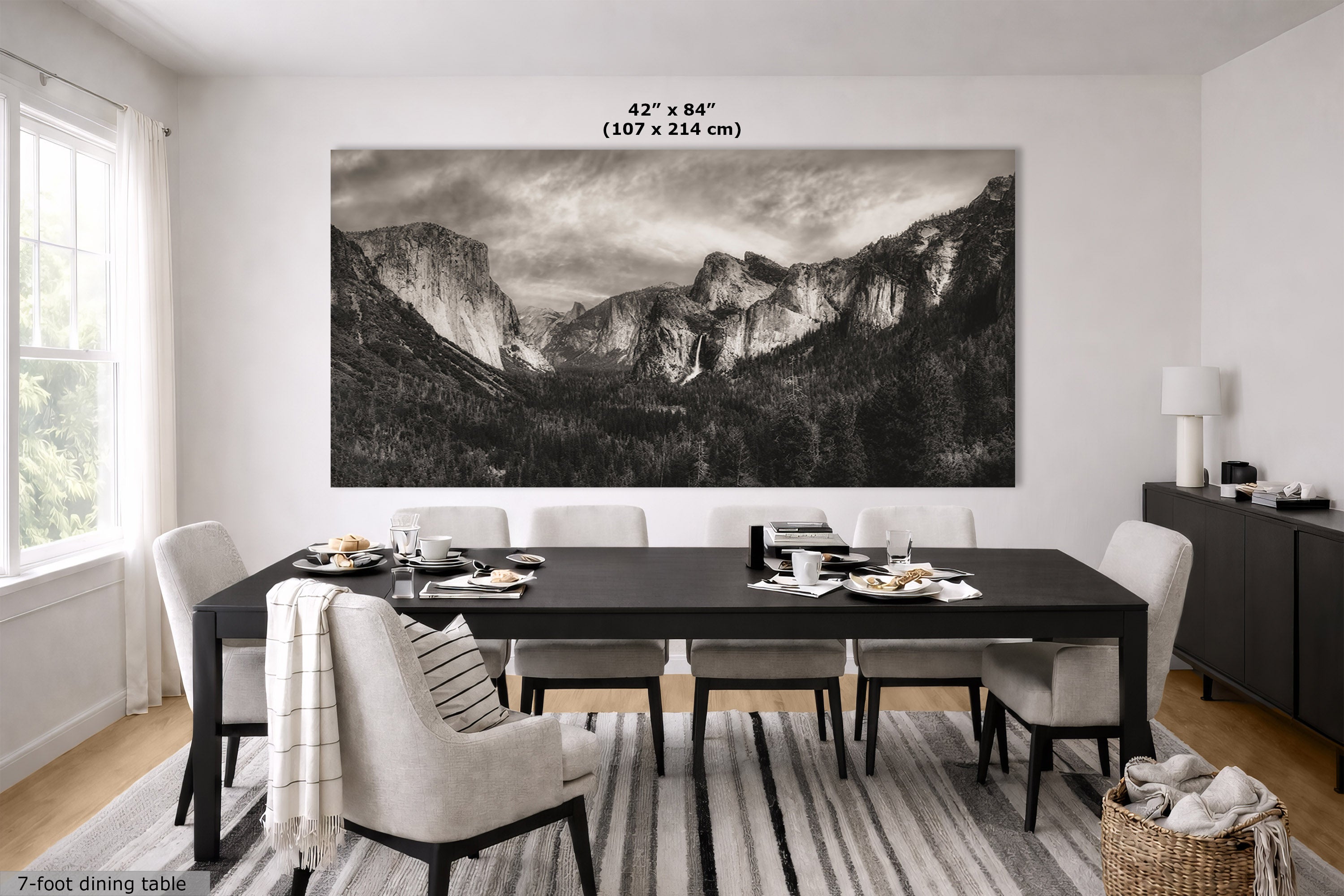 A large black and white landscape wall art print depicting a mountain valley, displayed above a dark dining table in a bright, modern dining room. The image includes a size measurement overlay at the top of the print.