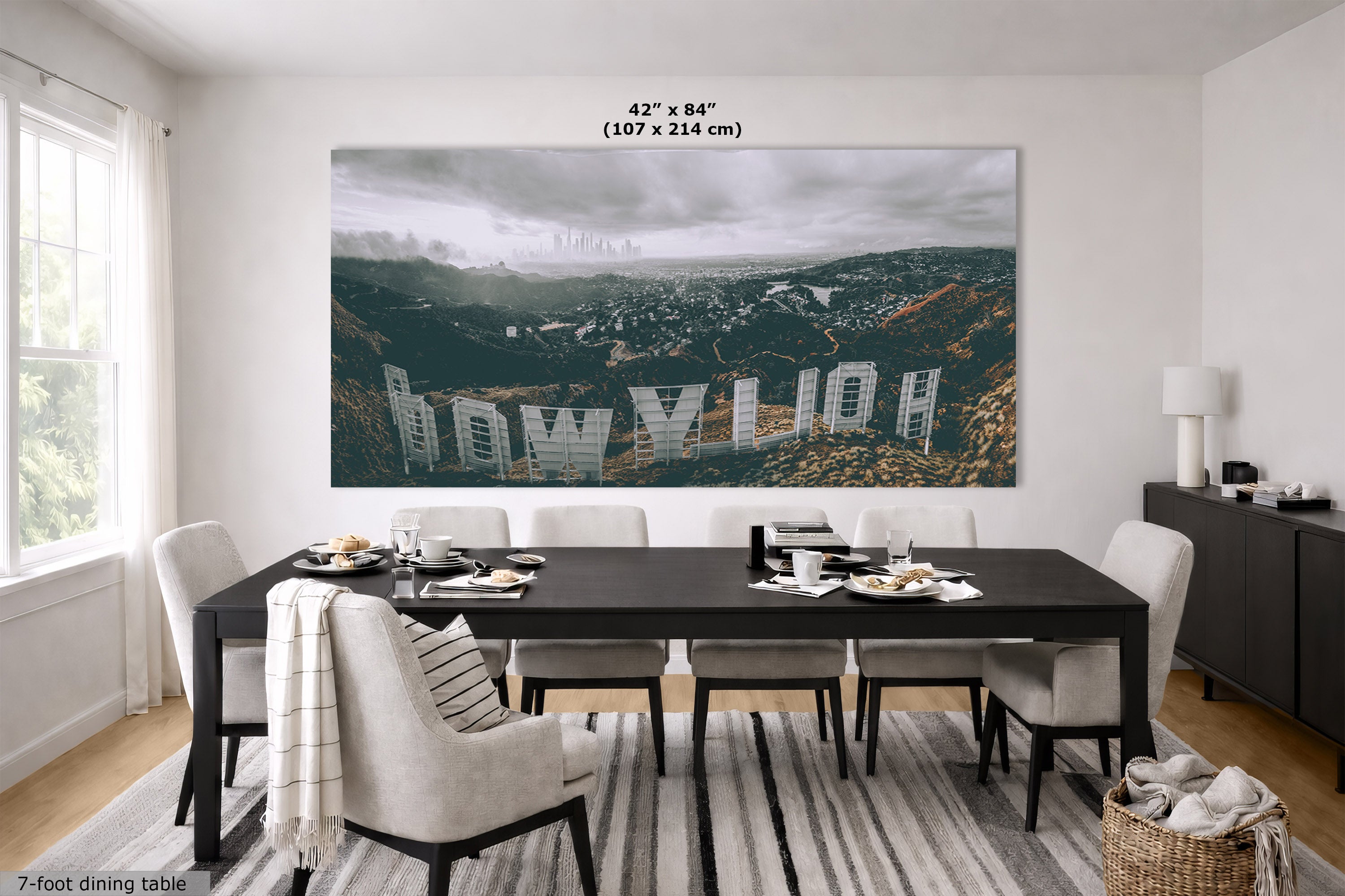 A large rectangular wall art print showing an aerial view of the Hollywood sign over a mountain landscape, displayed above a dining table in a modern dining room. The print includes the text 'HOLLYWOOD' and size information at the top.